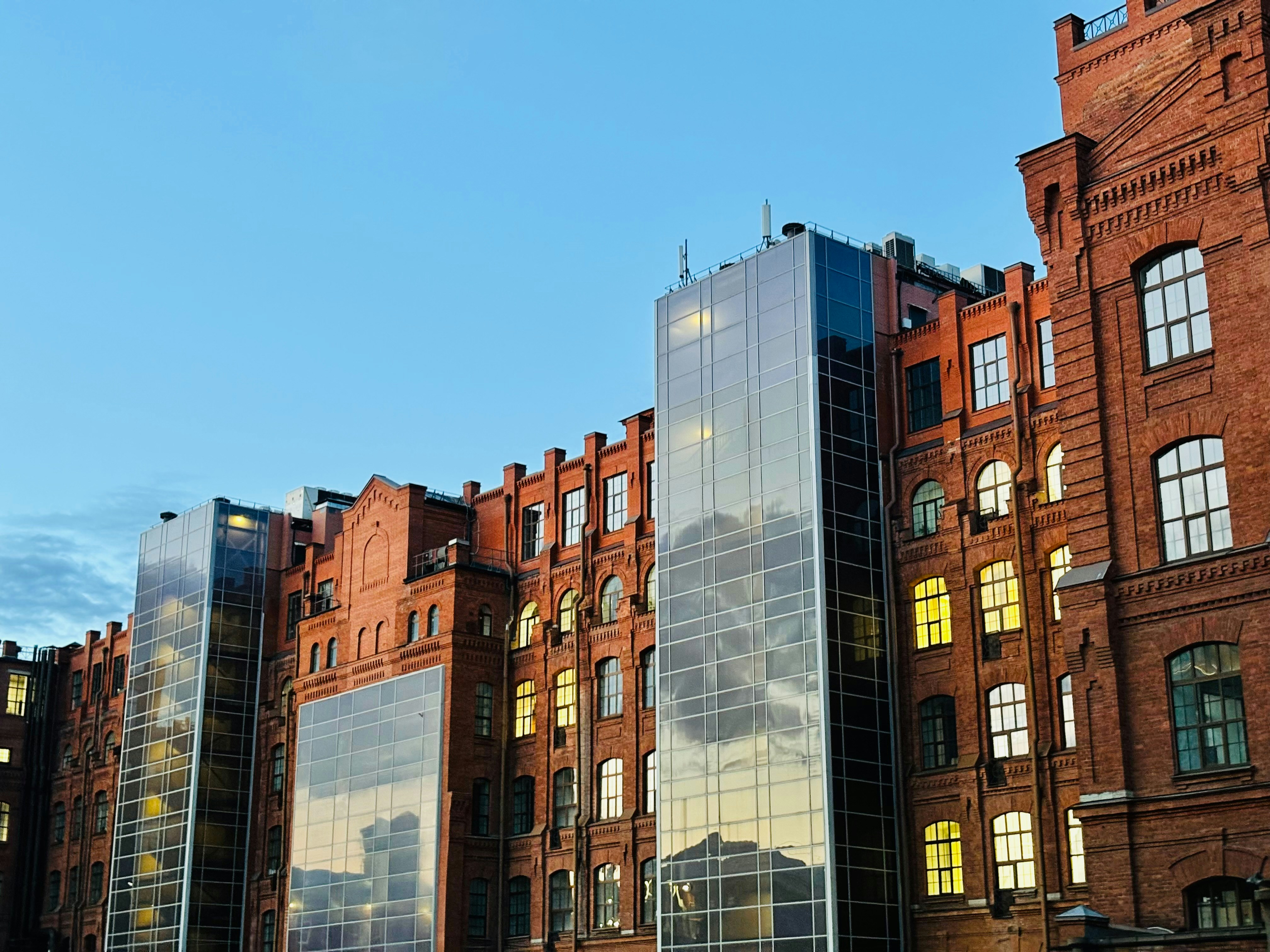 A red brick building with modern glass elevator shafts against a clear blue sky