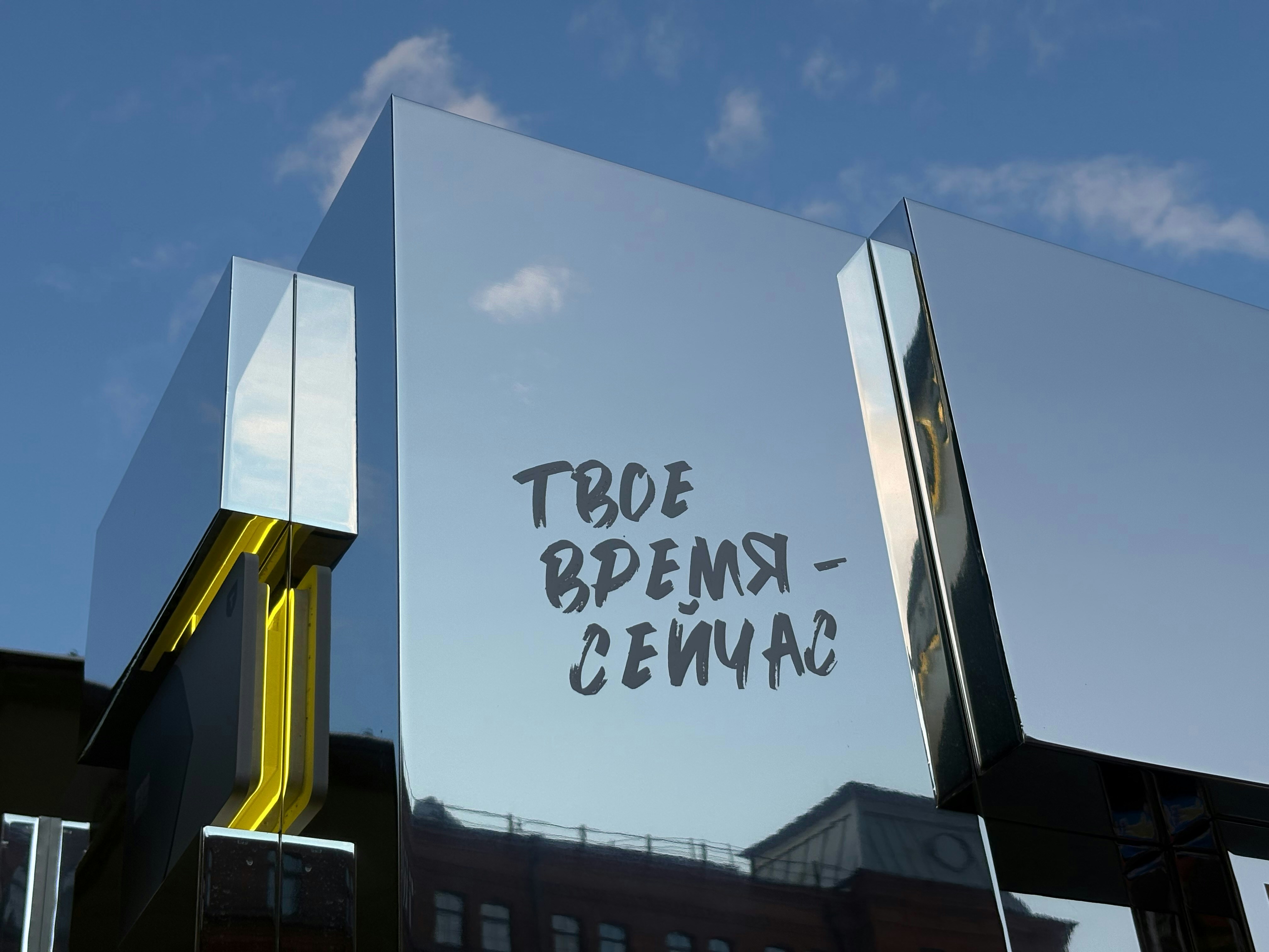 A mirrored cube with yellow accents and text reading "ТВОЕ ВРЕМЯ - СЕЙЧАС" outdoors