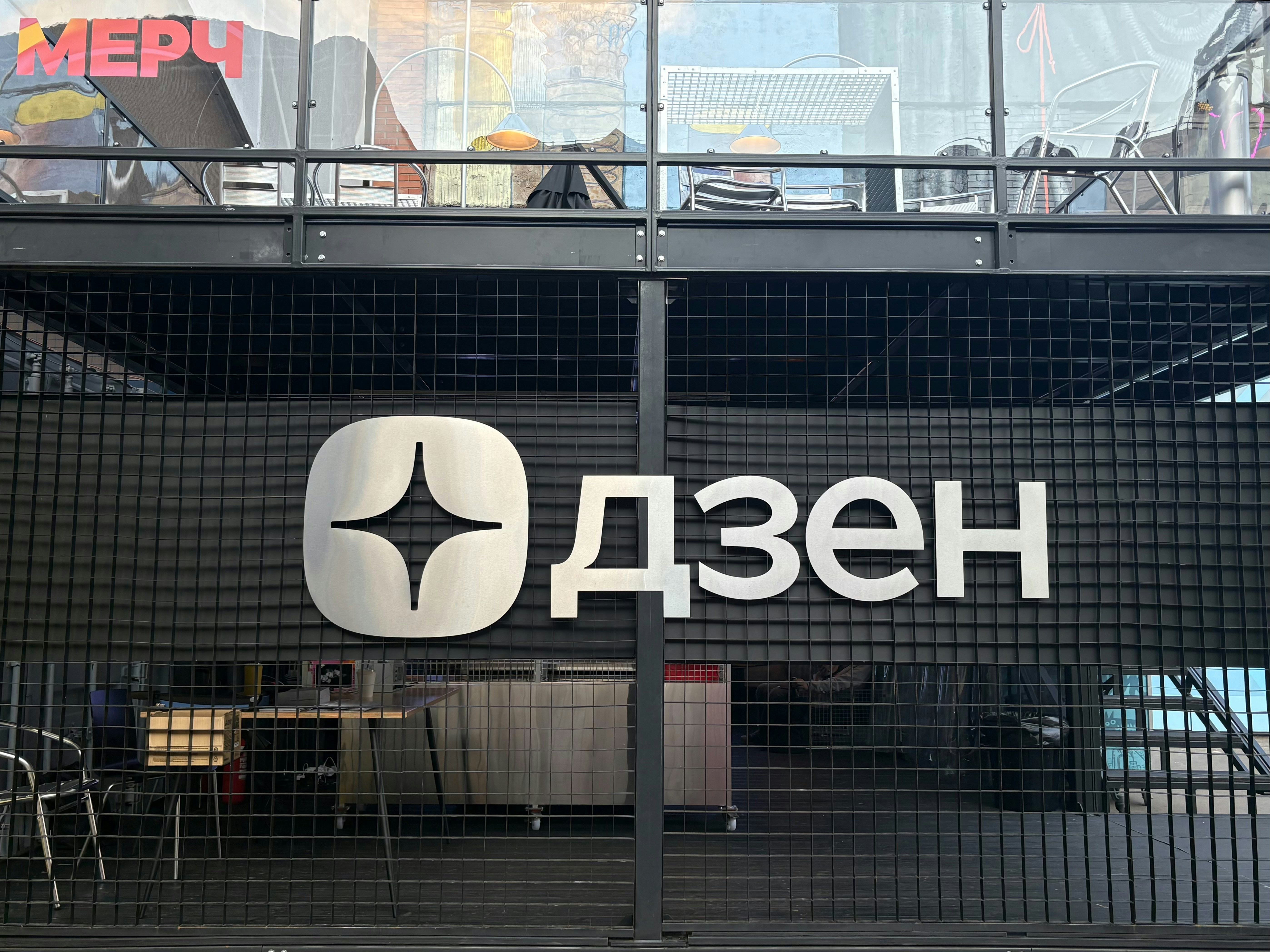 A metal logo reading "Дзен" on a black grid wall of a building