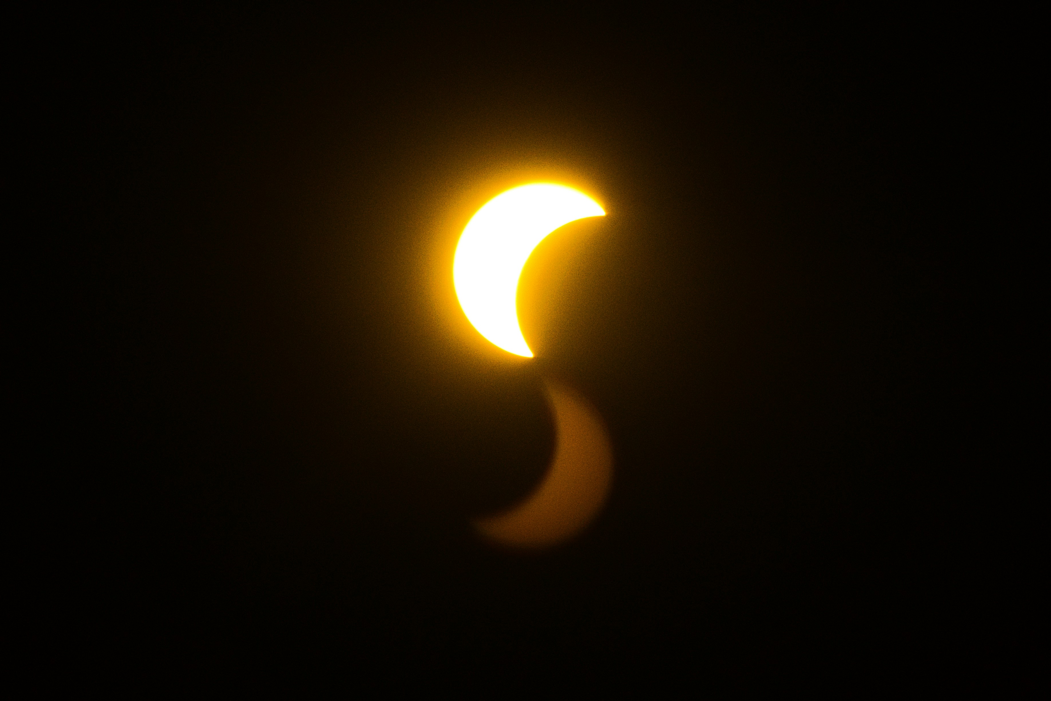 A bright crescent sun with a faint reflection against a black sky.