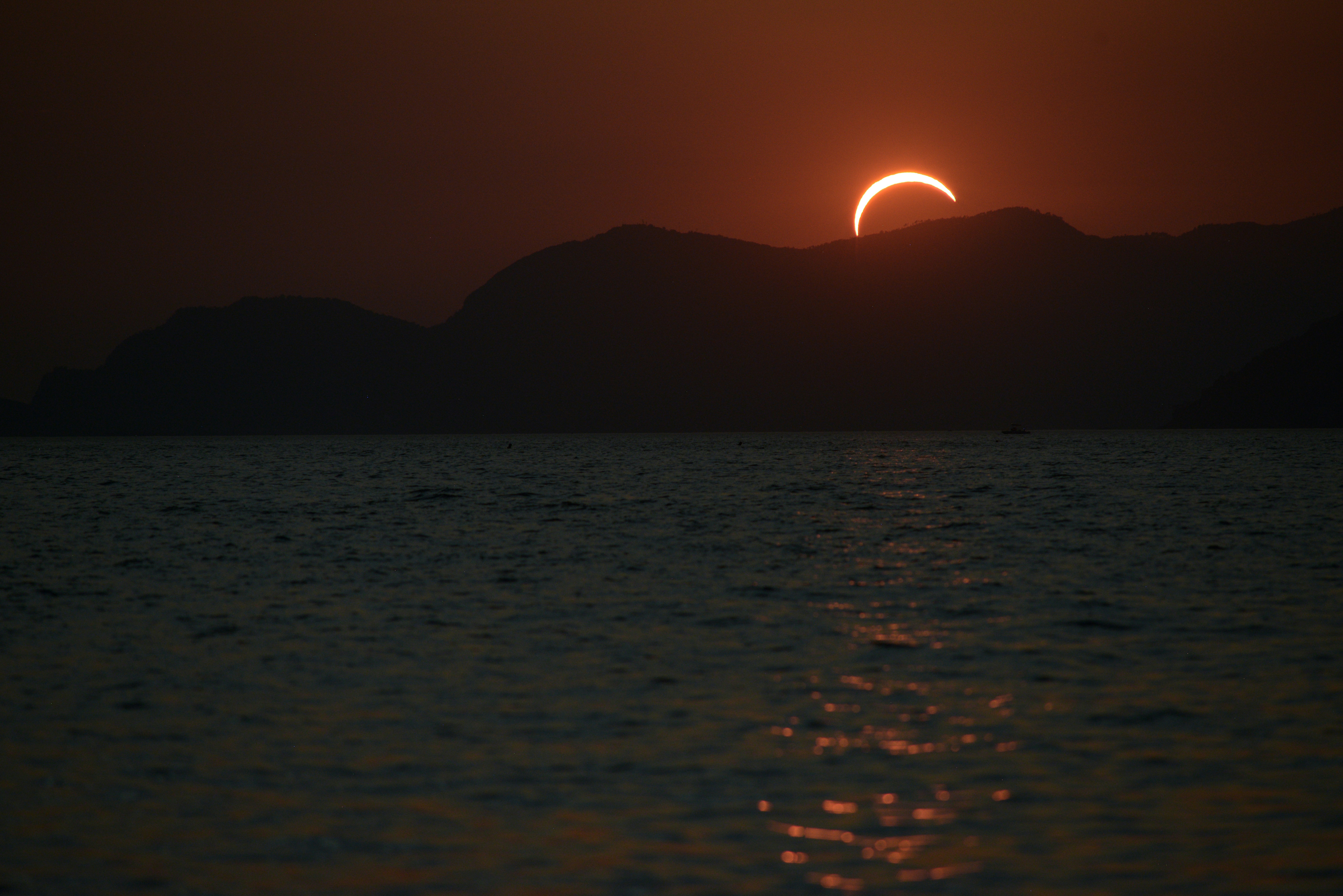 A solar eclipse above dark mountains and the rippling surface of the sea