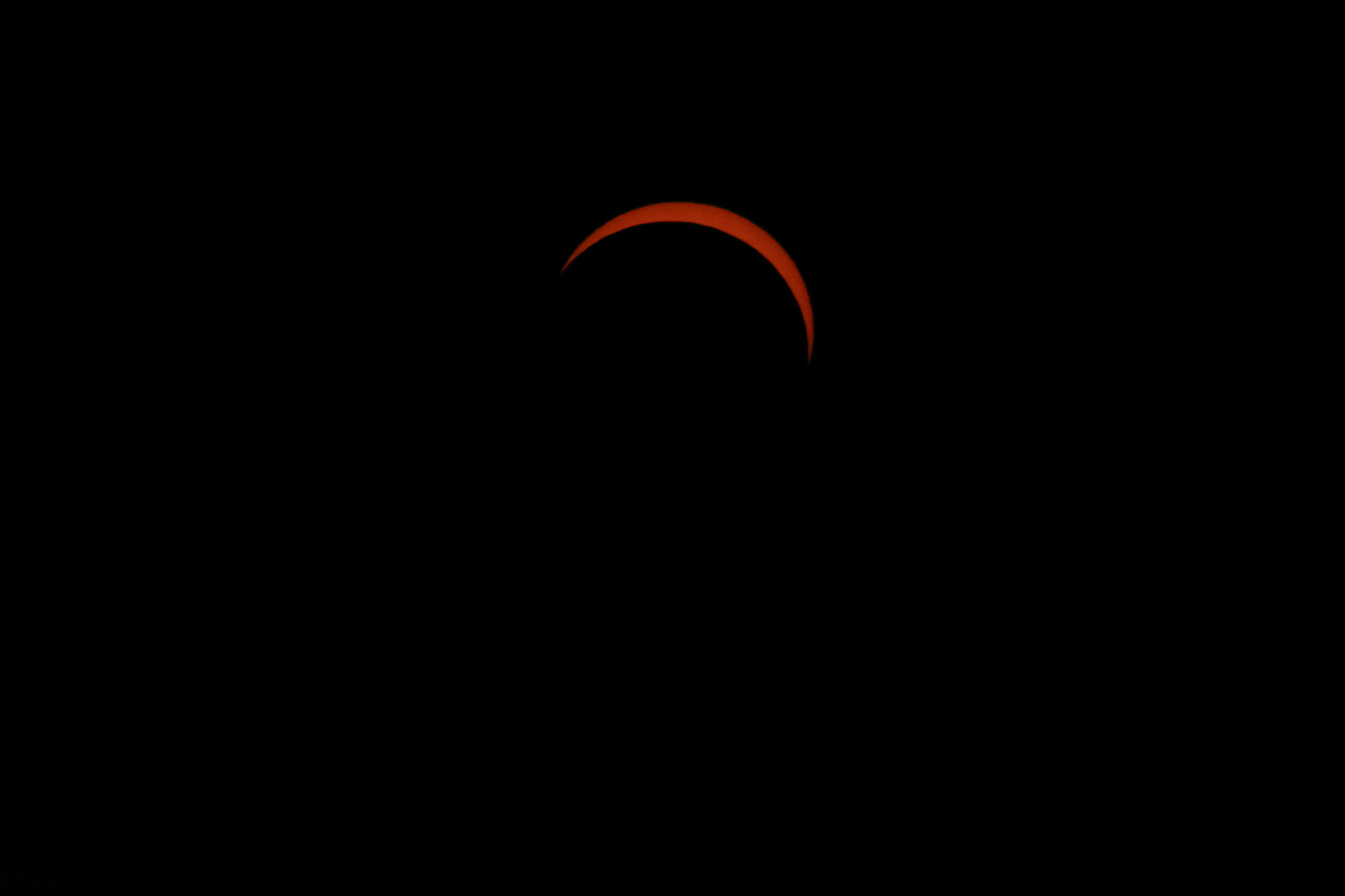 A thin glowing red crescent of the sun during a solar eclipse
