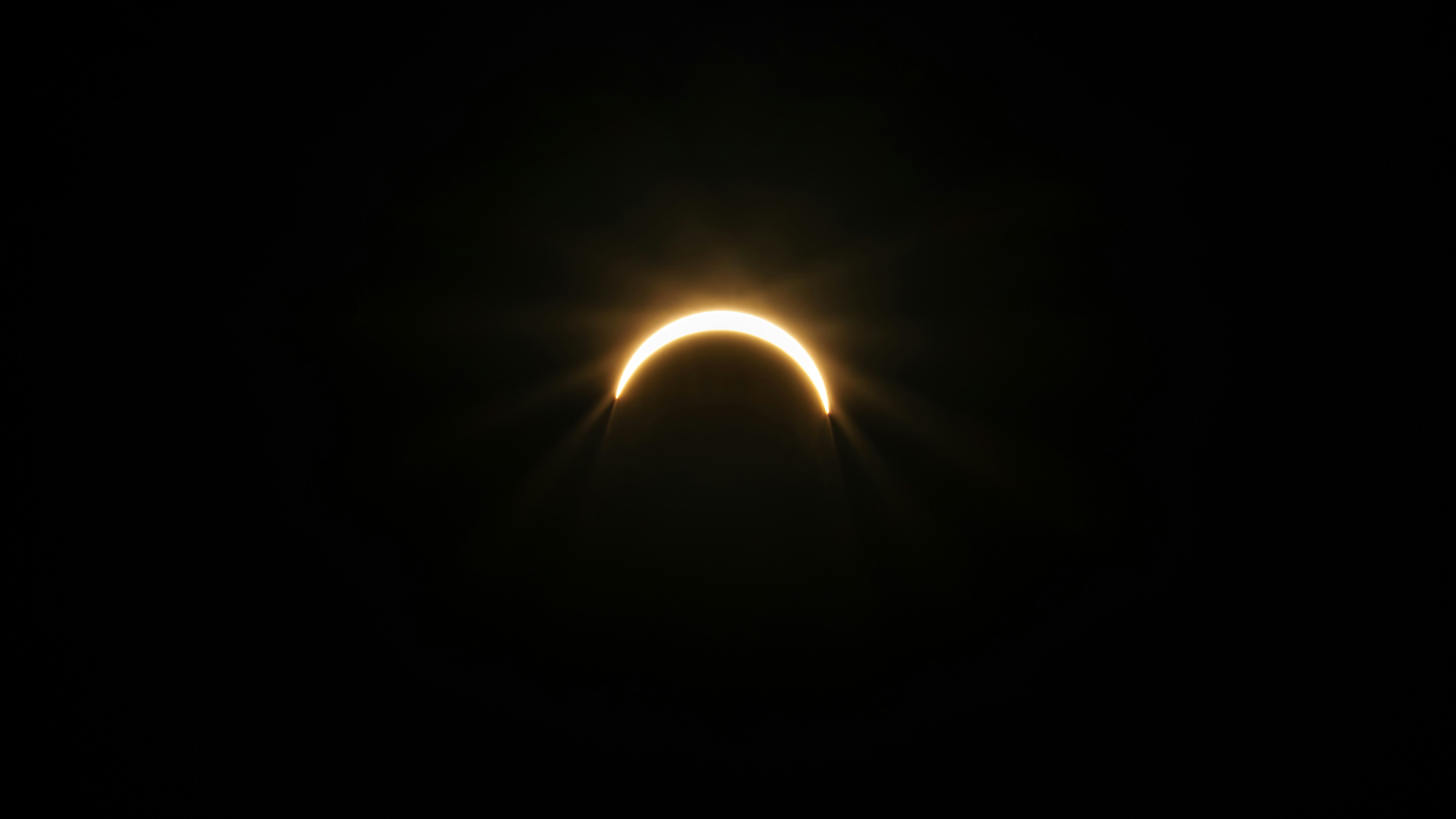 A bright crescent of light from a solar eclipse against a black sky.