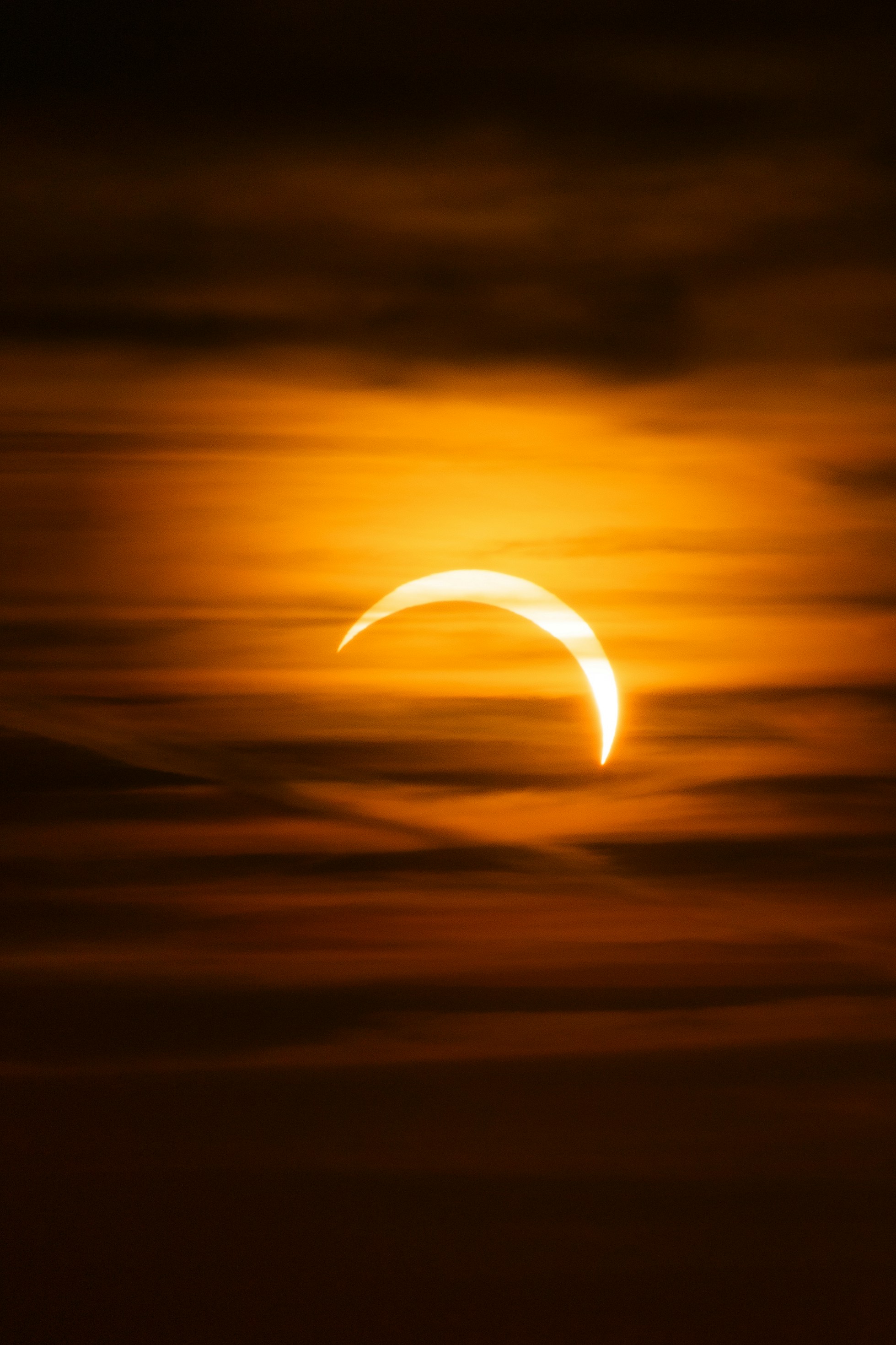 A partial solar eclipse glowing through dark orange clouds in the sky.
