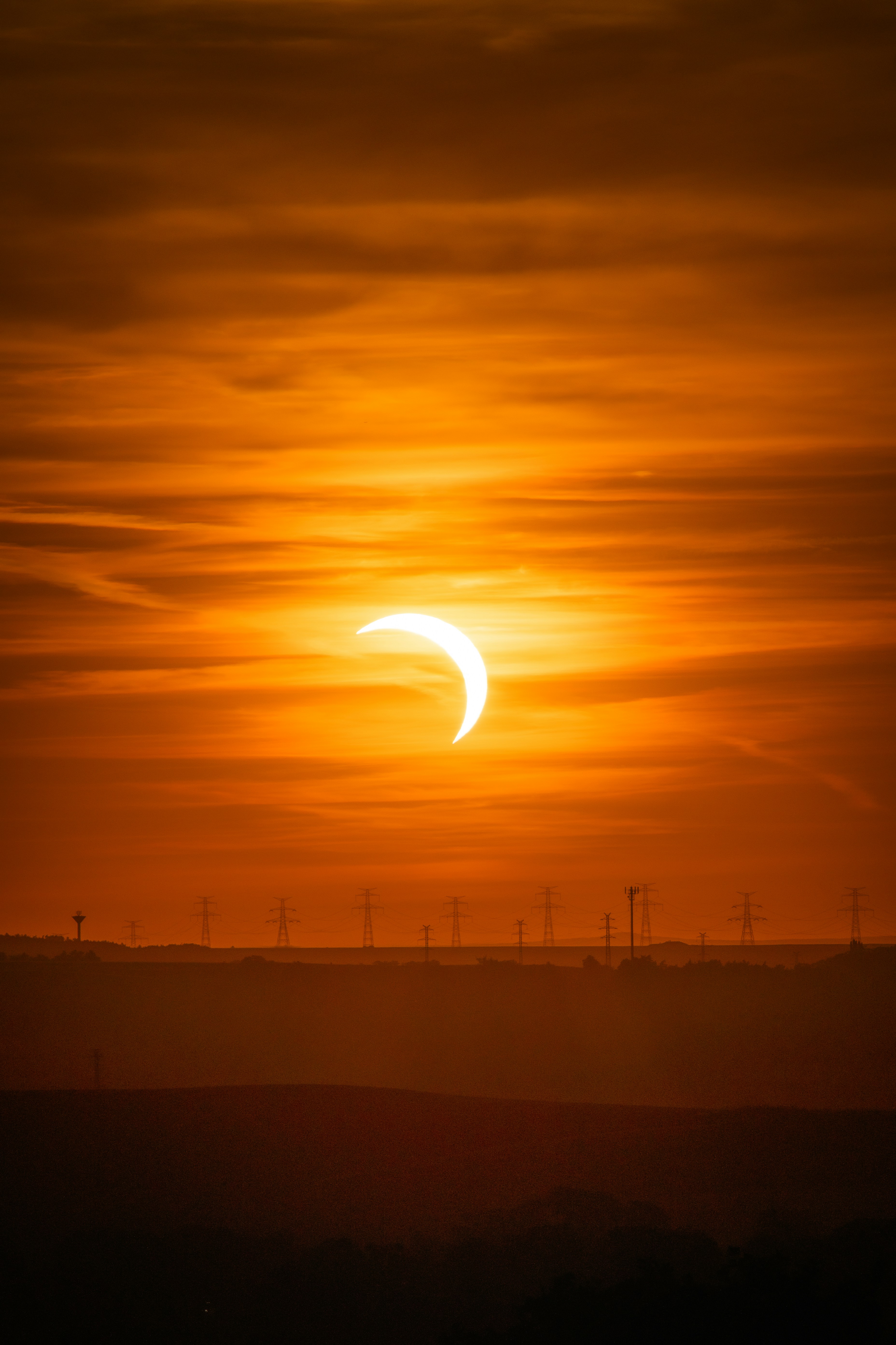 A partial solar eclipse in a warm orange sky above distant electrical pylons.