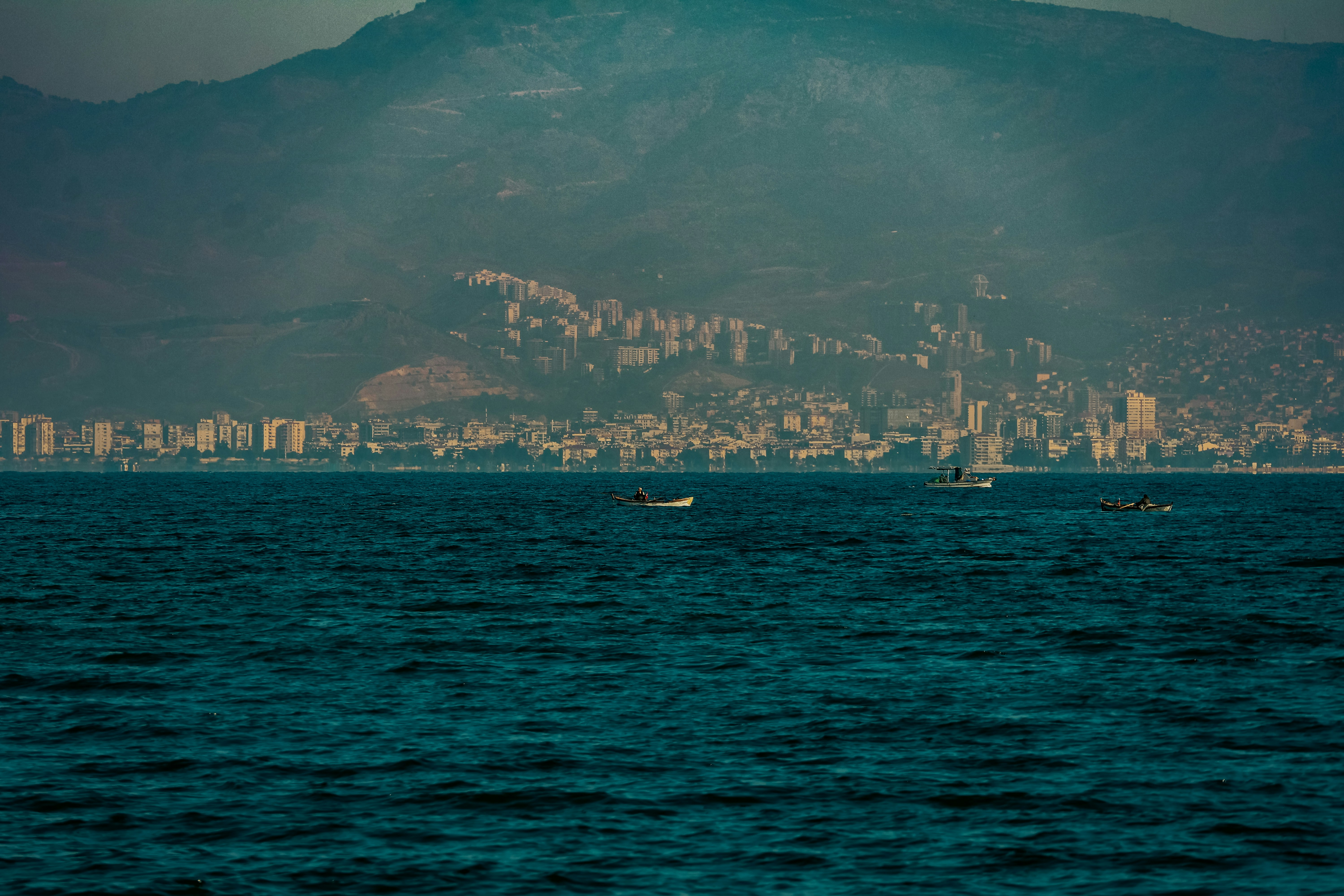 Small fishing boats on dark water before a coastal city and mountain range