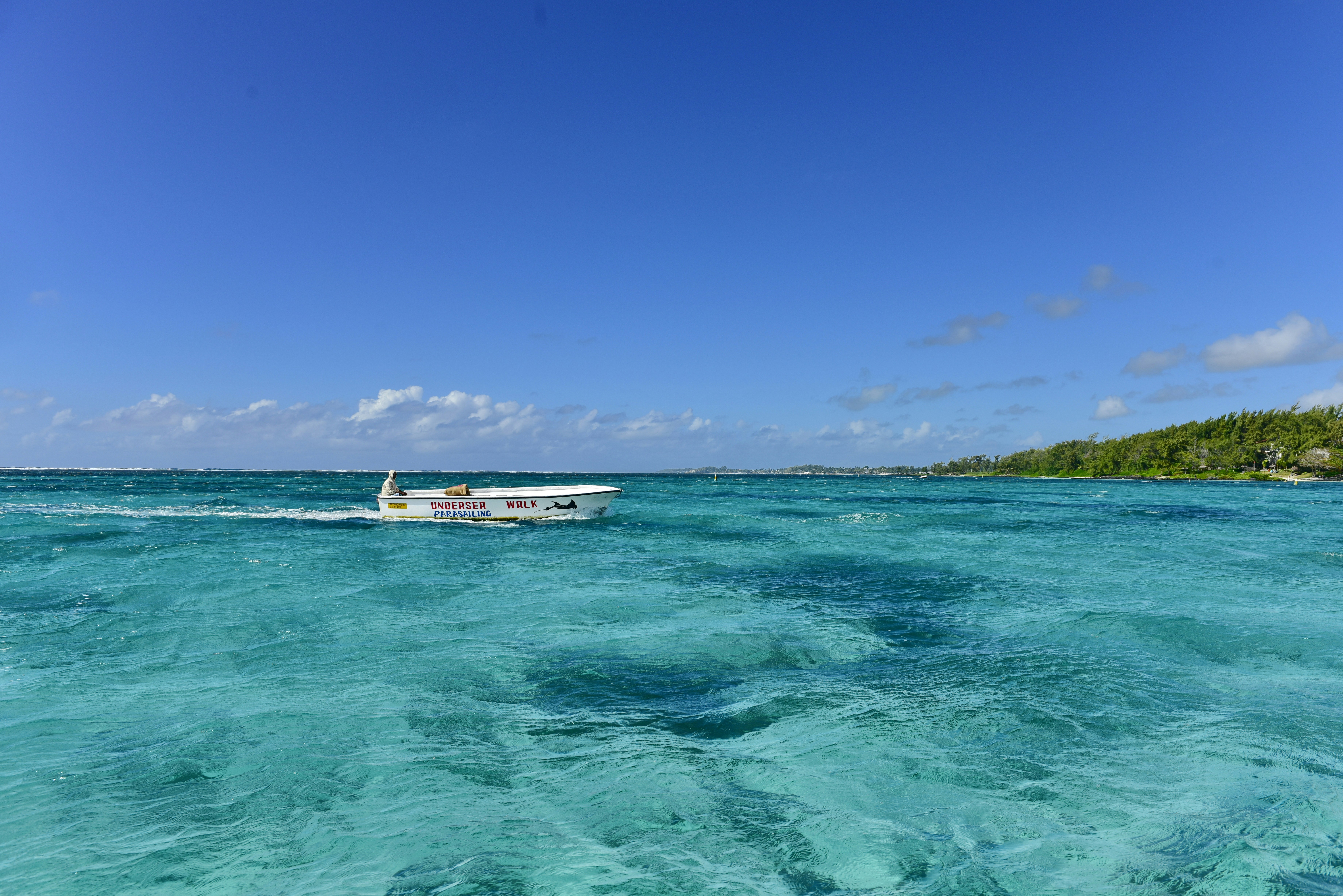 A small white motorboat moving across clear turquoise water under a blue sky