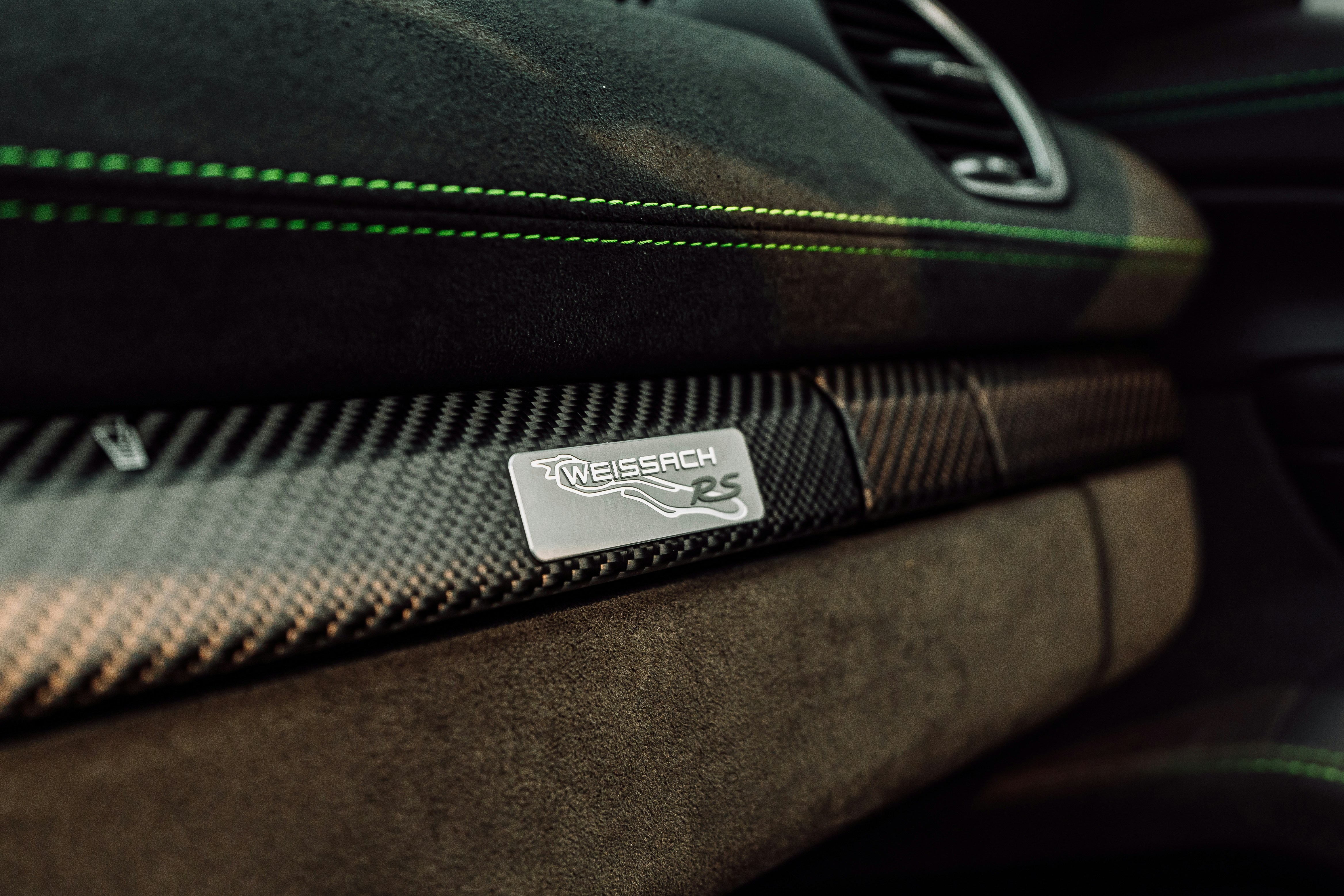 A carbon fiber dashboard trim with a Weissach RS badge and green stitching