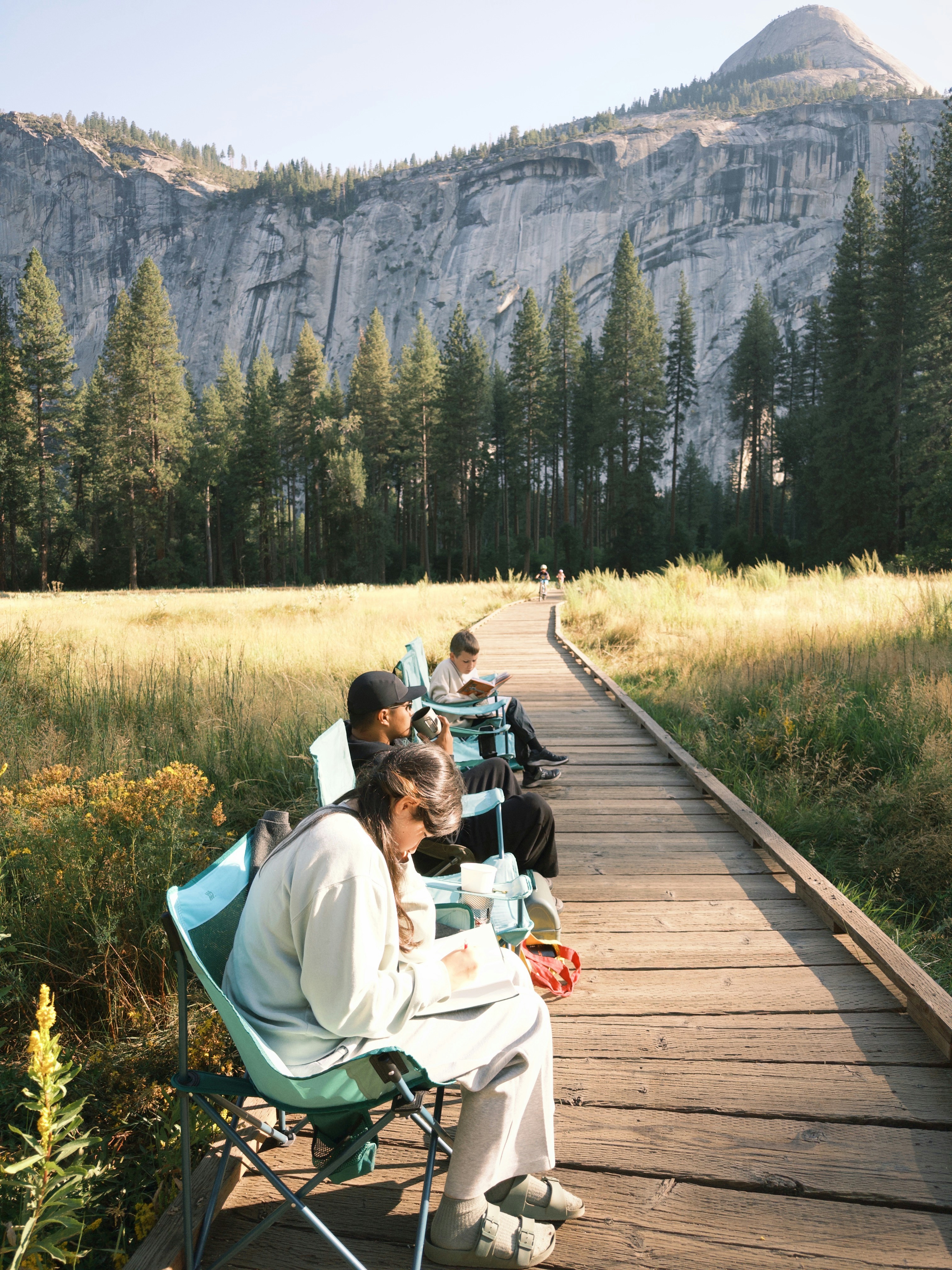 Tiga orang duduk di kursi lipat di atas papan kayu di Taman Nasional Yosemite.
