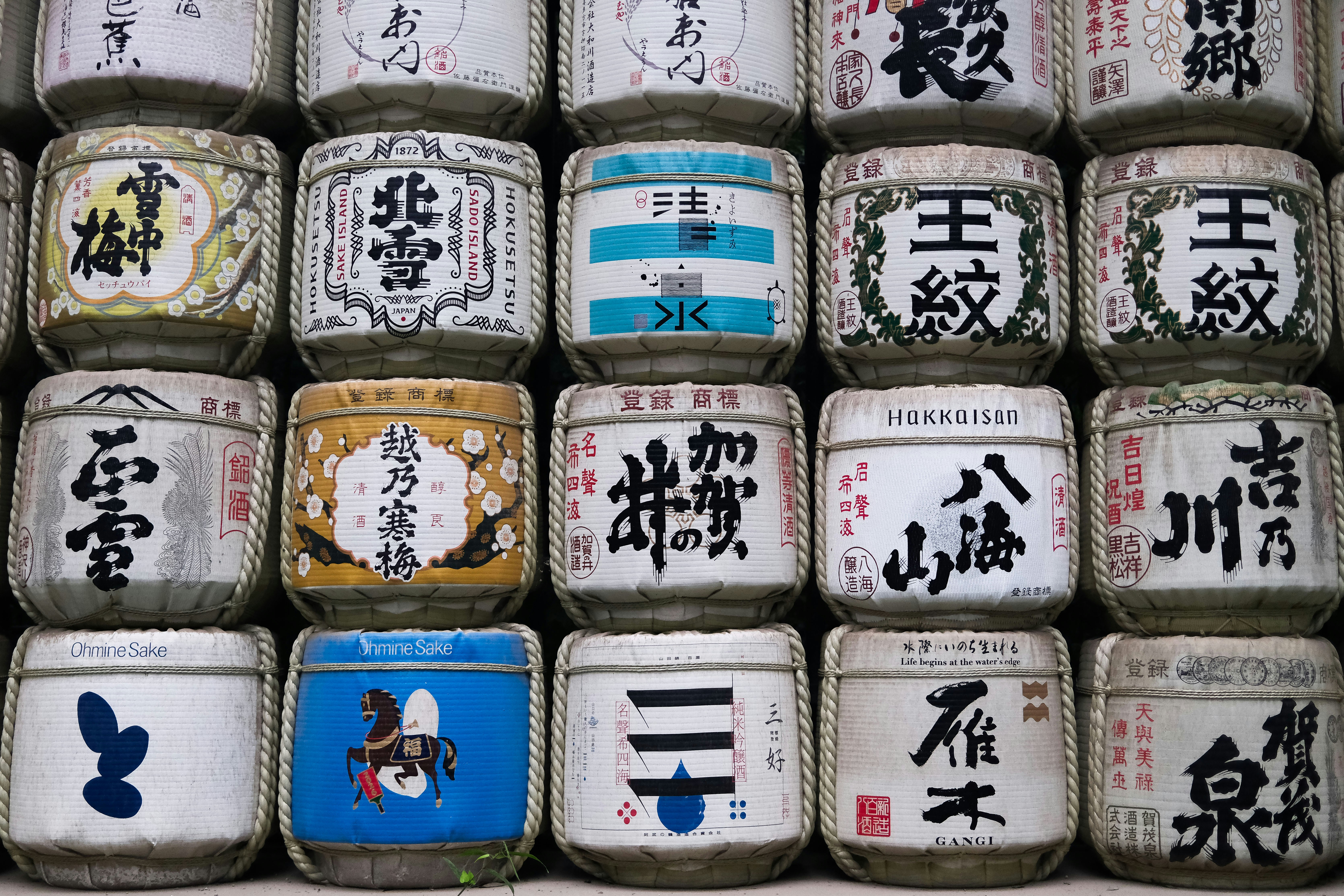 A wall of stacked sake barrels with various Japanese calligraphy and colorful graphic designs