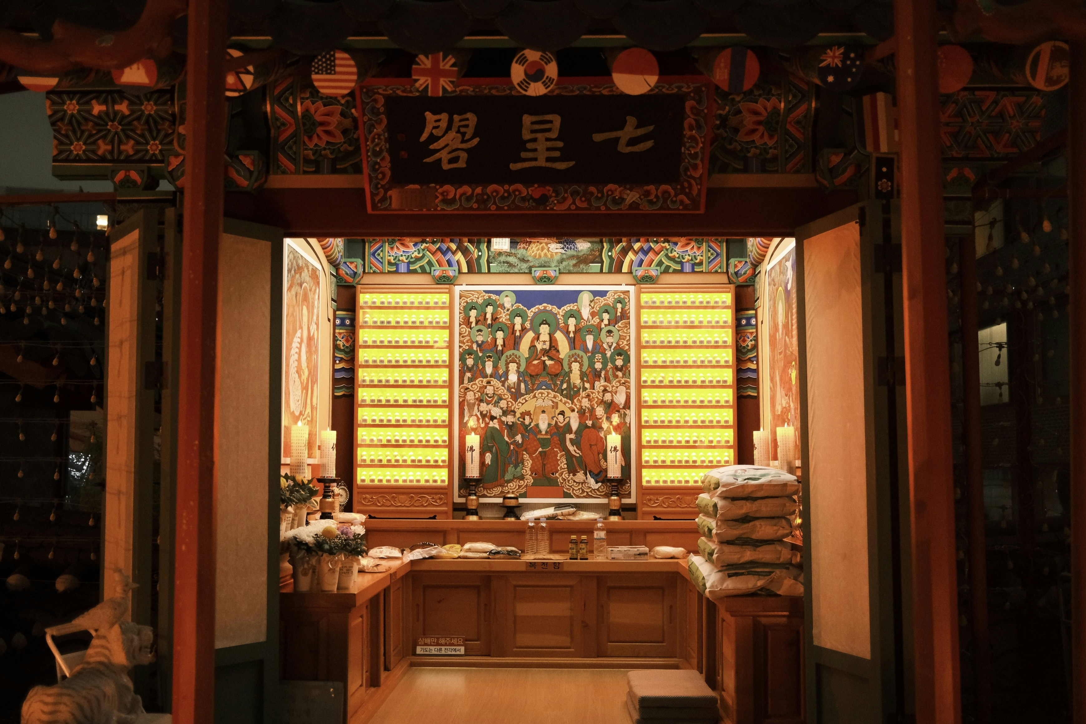 An illuminated Buddhist shrine with a central painting and rows of small votive lights