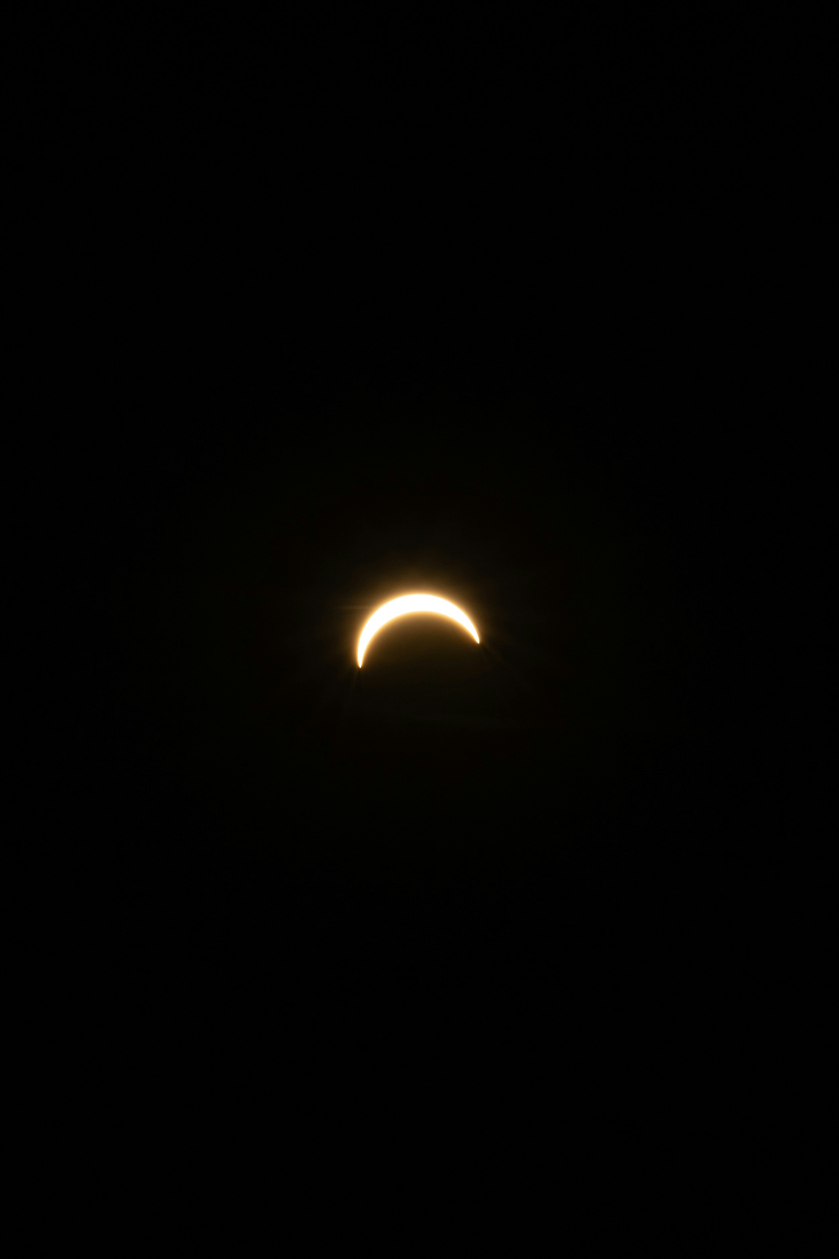 A bright crescent sun partially obscured by the moon against a black sky.