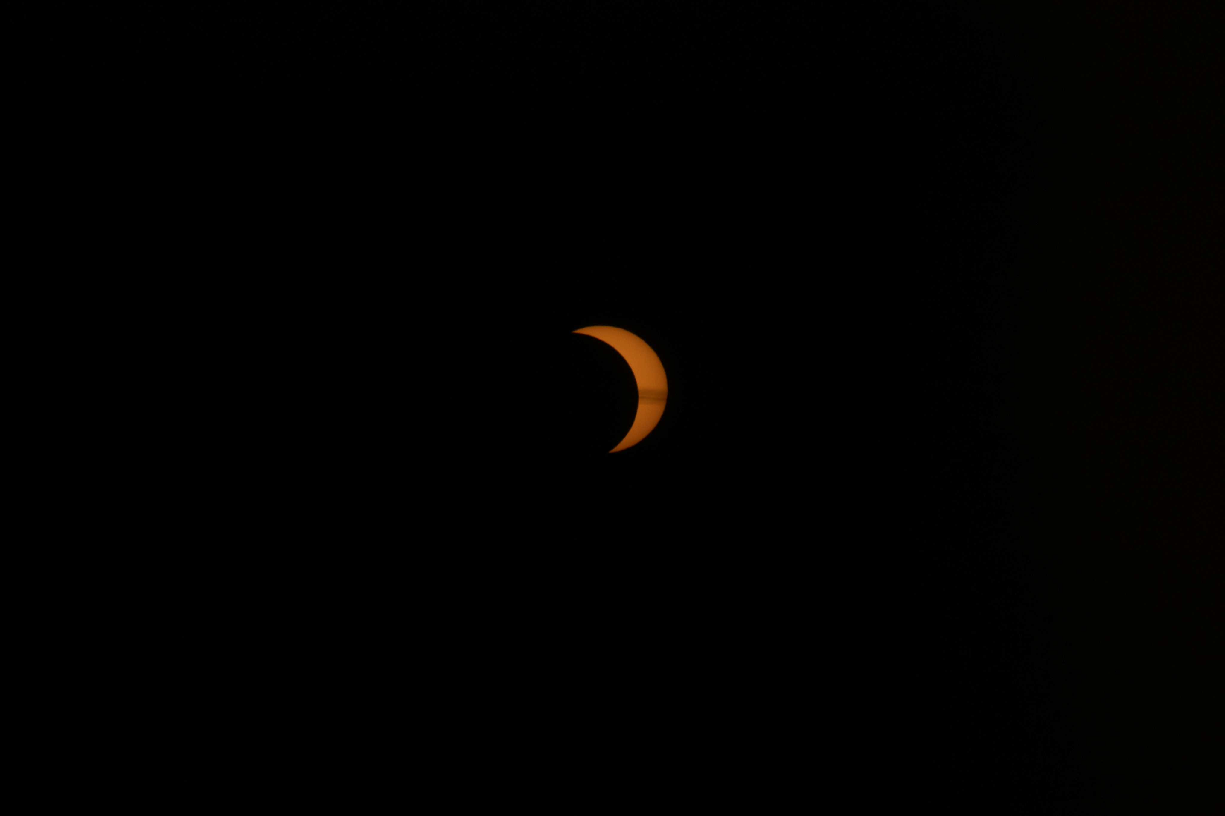 A crescent-shaped sun partially obscured by the moon against a dark sky.