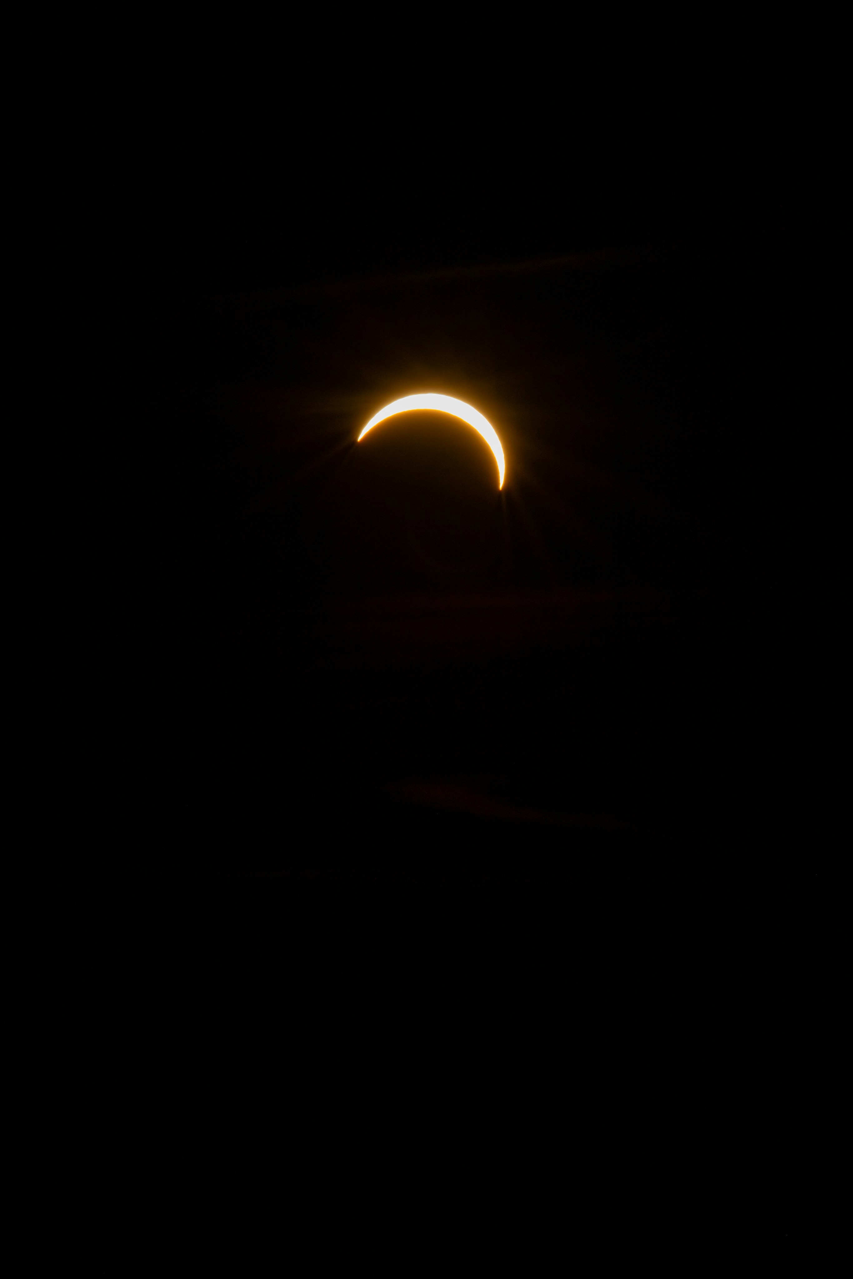 A thin crescent of the sun glowing against a dark black sky.