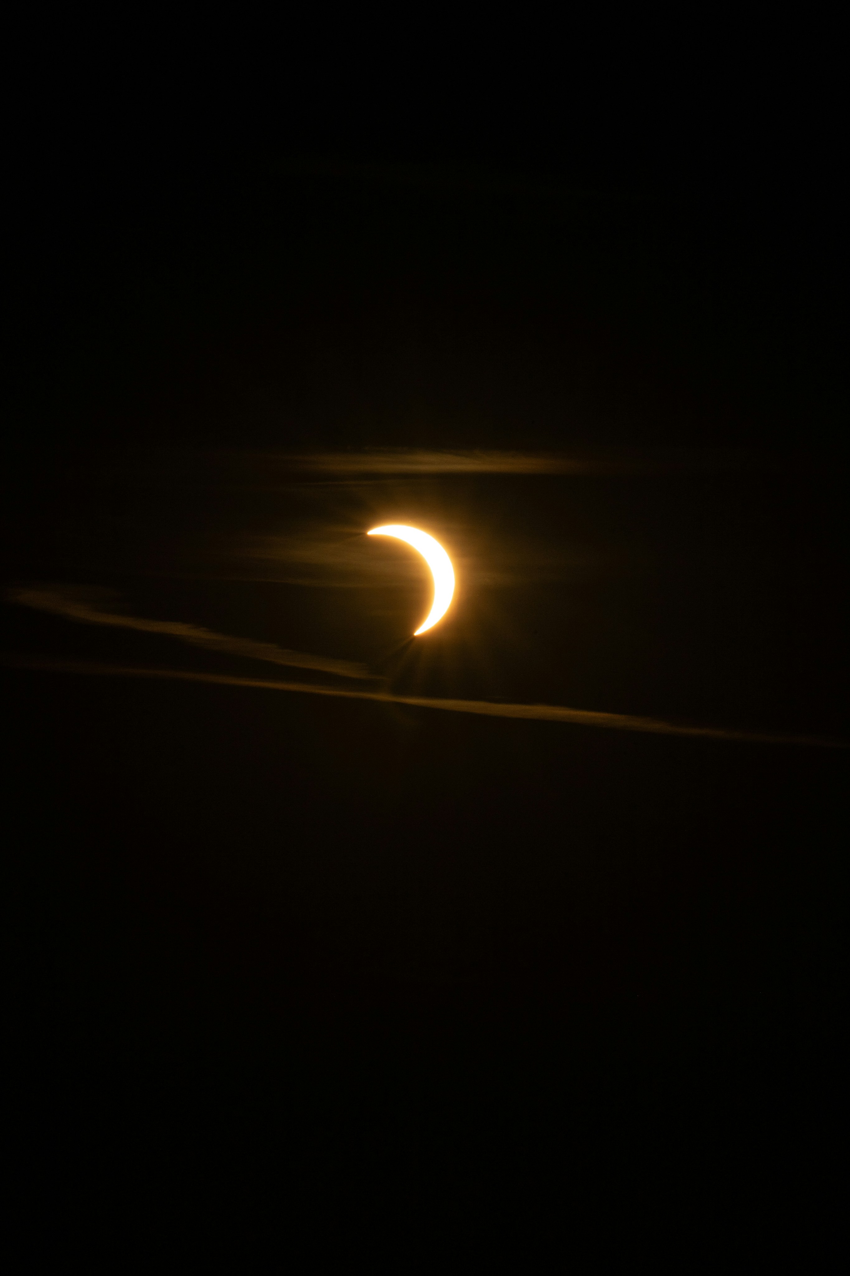 A crescent sun partially obscured by thin clouds in a dark sky.