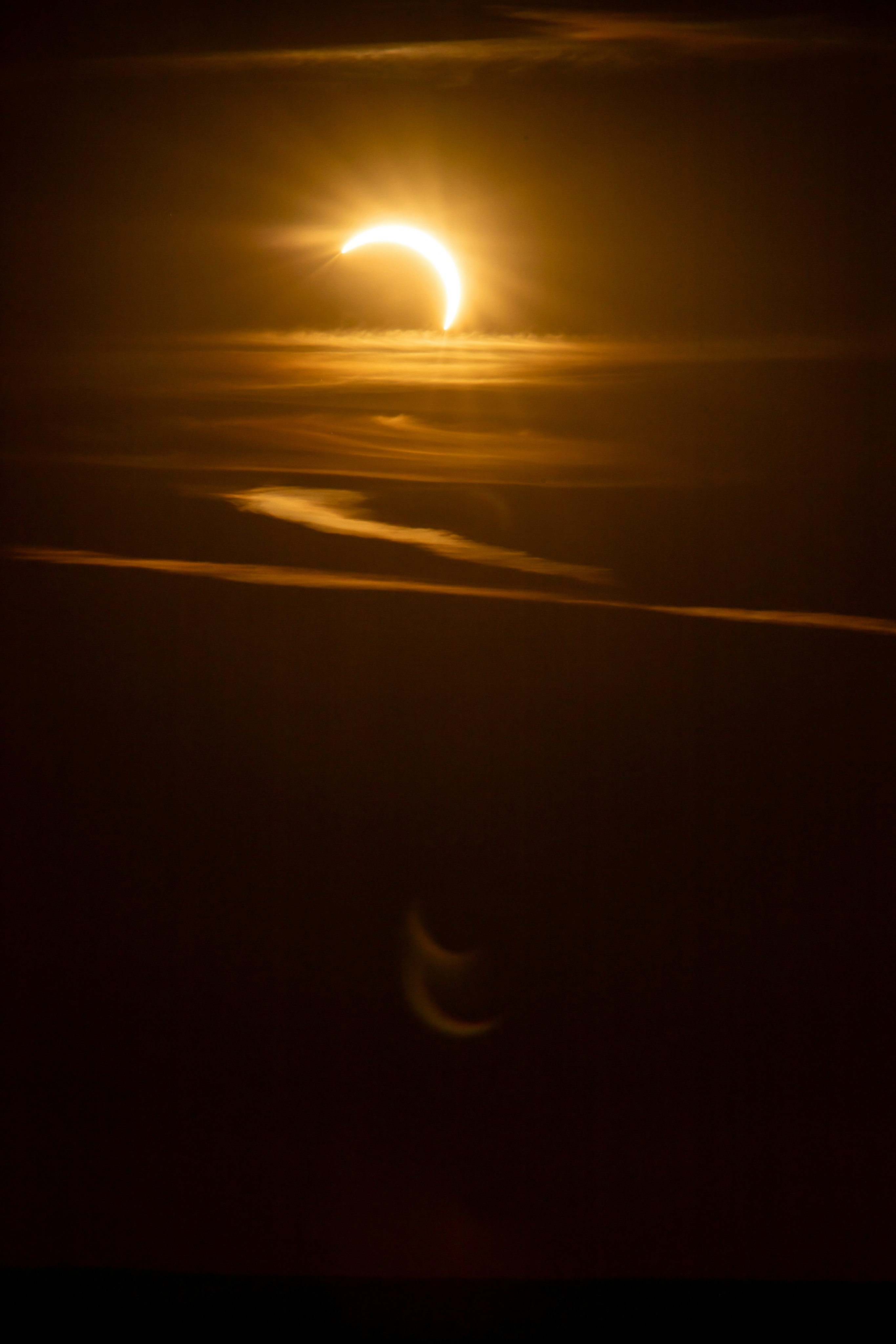 A partial solar eclipse glowing in a dark orange sky with thin clouds.