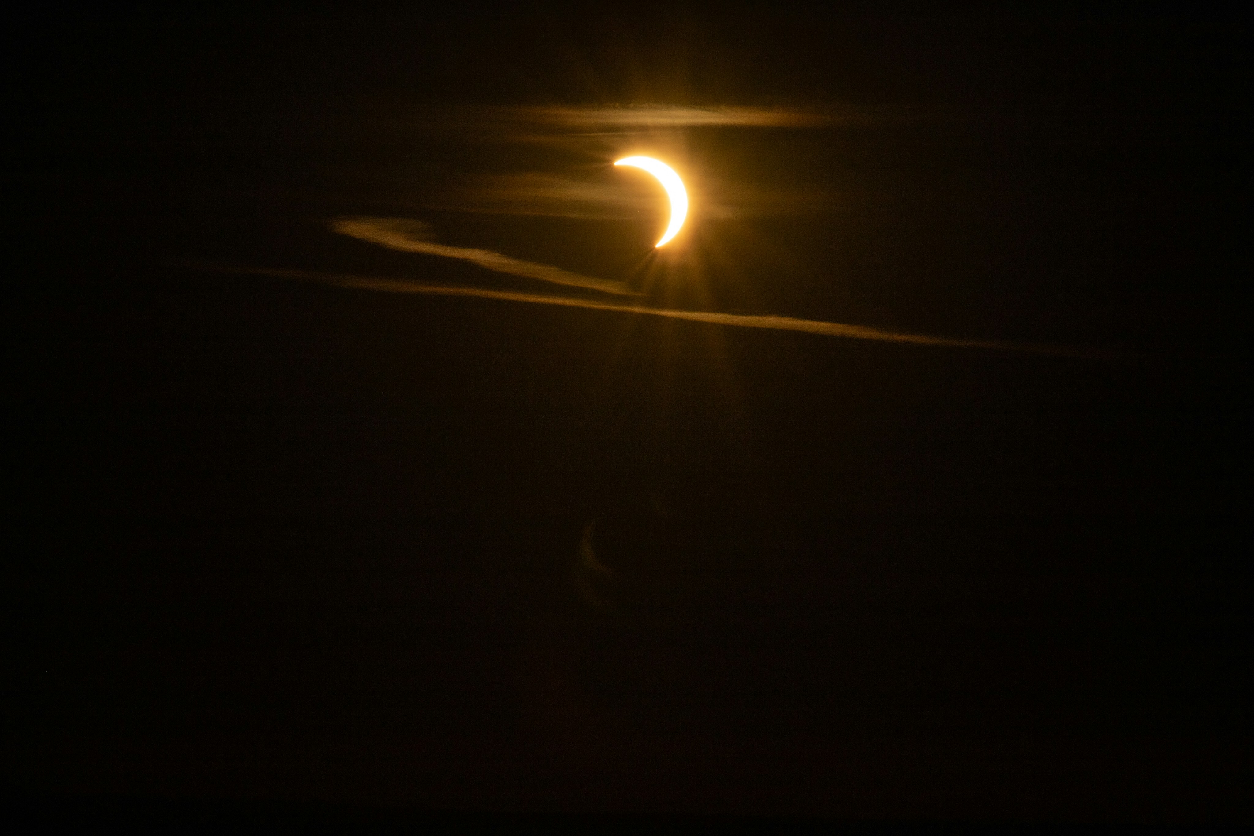 A crescent sun partially obscured by the moon in a dark sky.