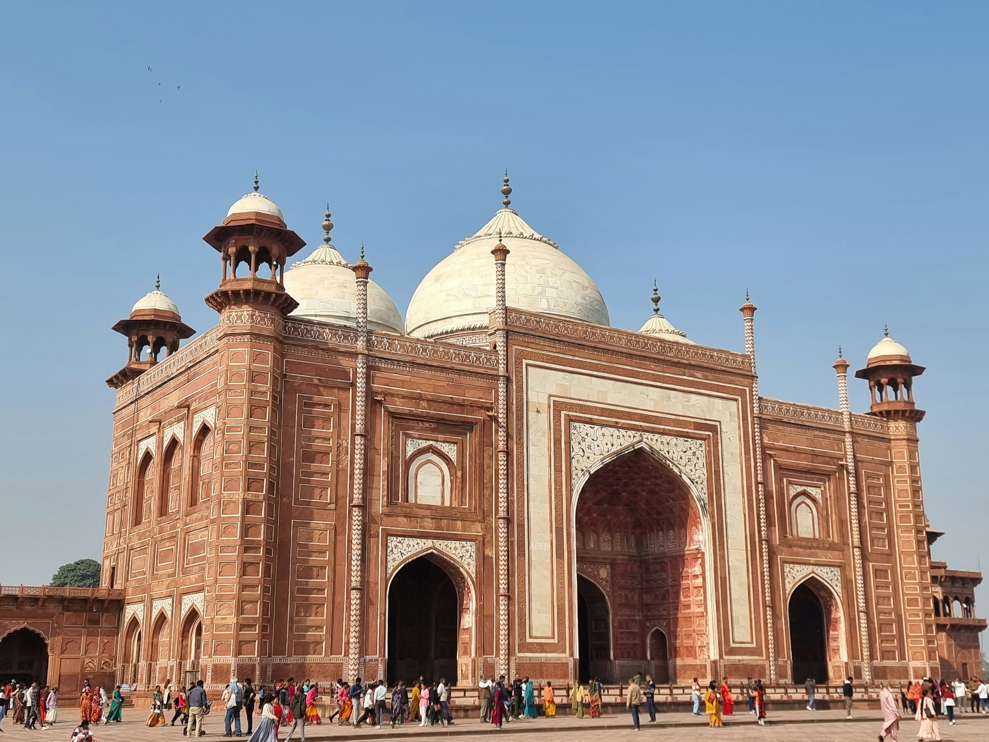 A crowd of people walking in front of the red sandstone Taj Mahal mosque.