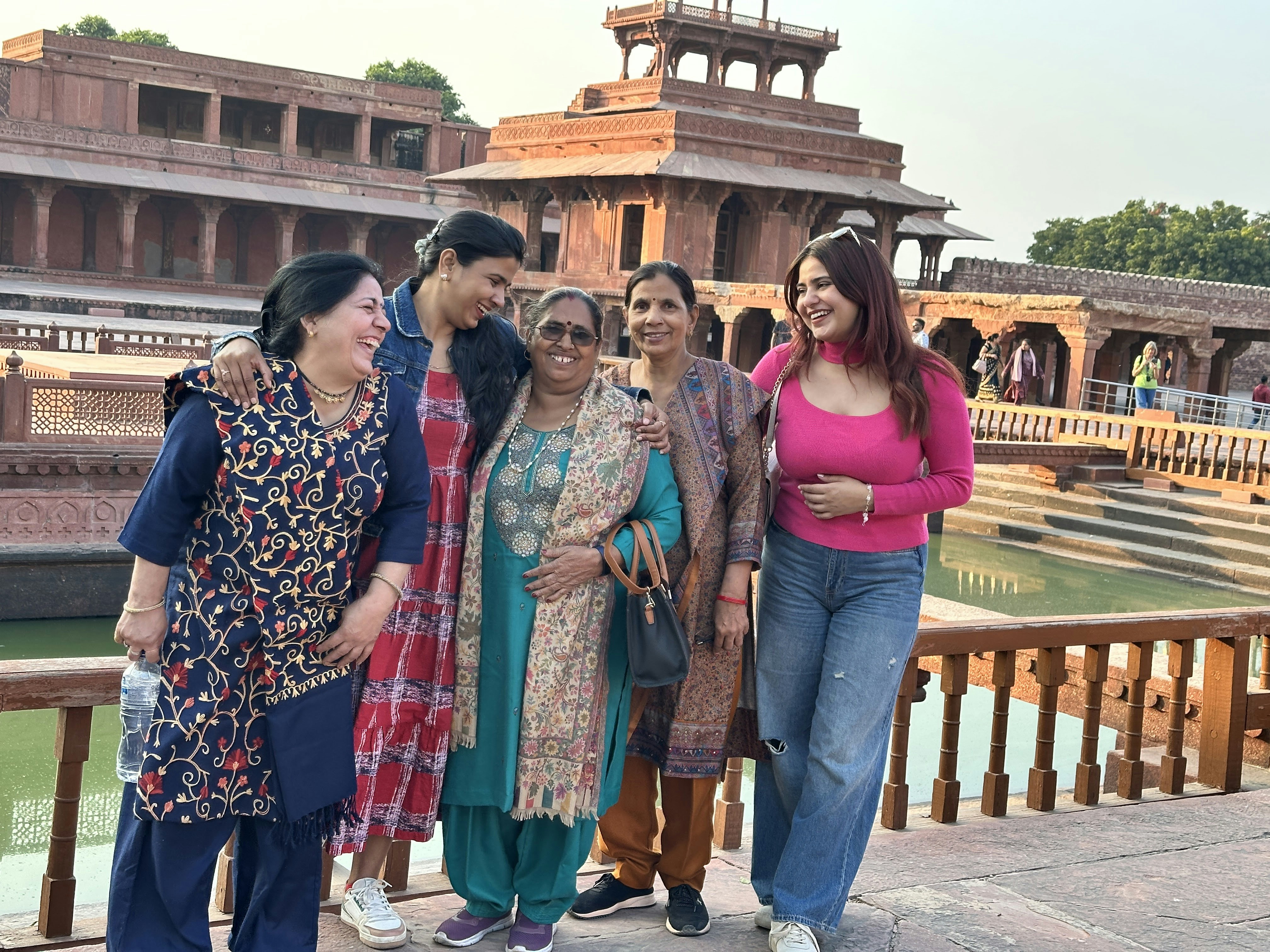 Five women laughing together in front of the red sandstone architecture of Fatehpur Sikri.