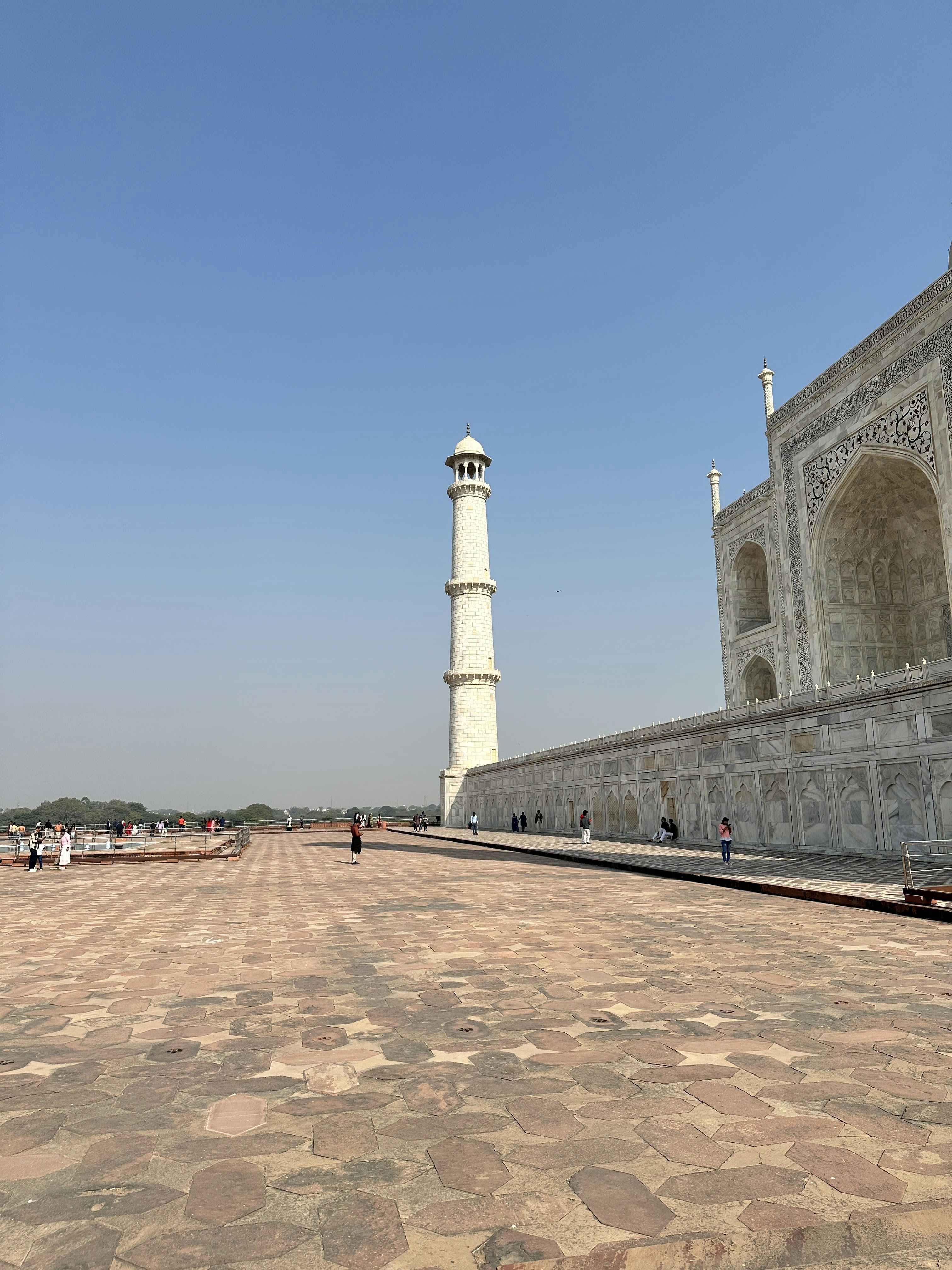 The Taj Mahal minaret and marble wall above a stone plaza in Agra.