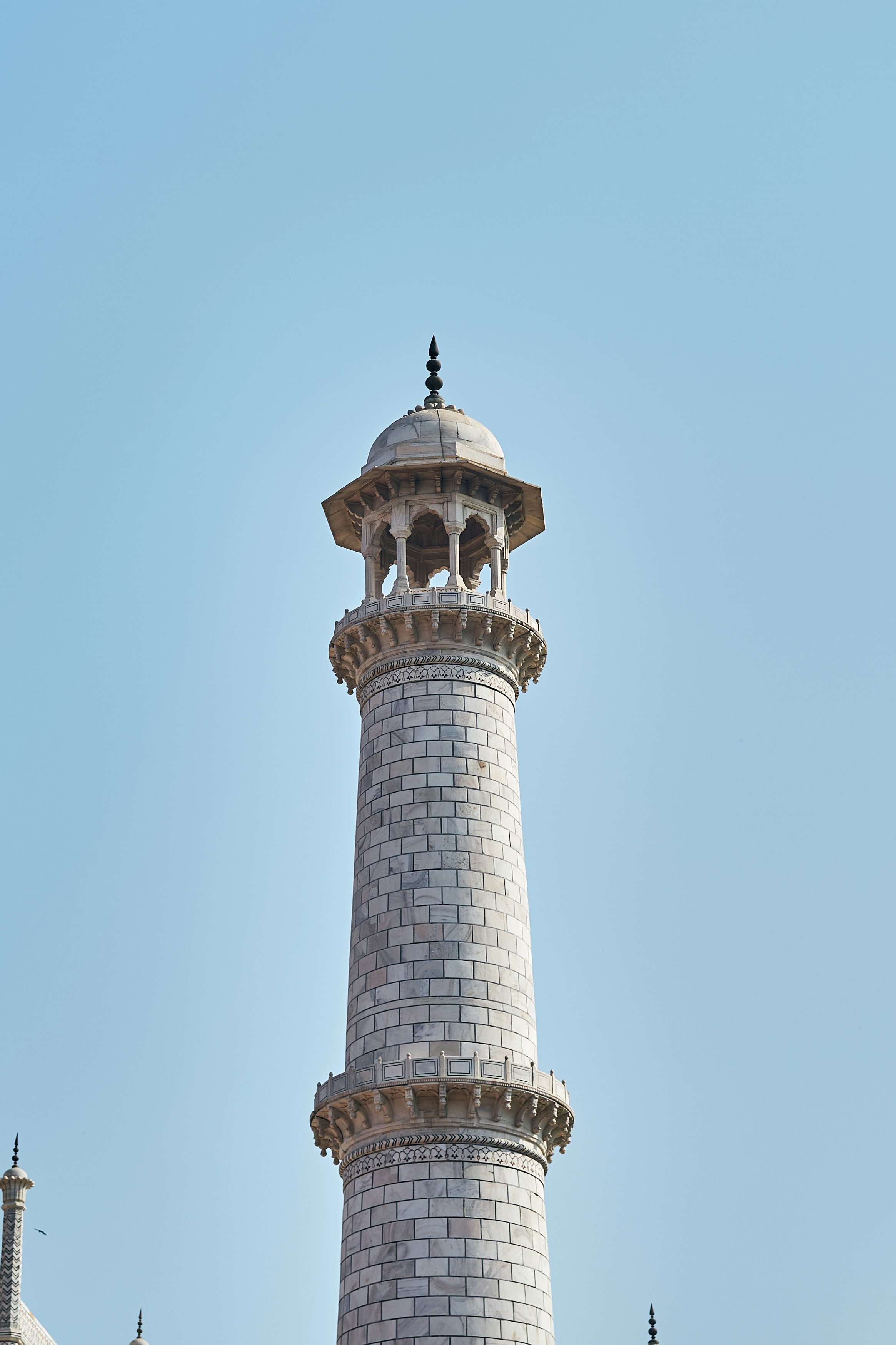 A white marble minaret of the Taj Mahal against a clear blue sky.