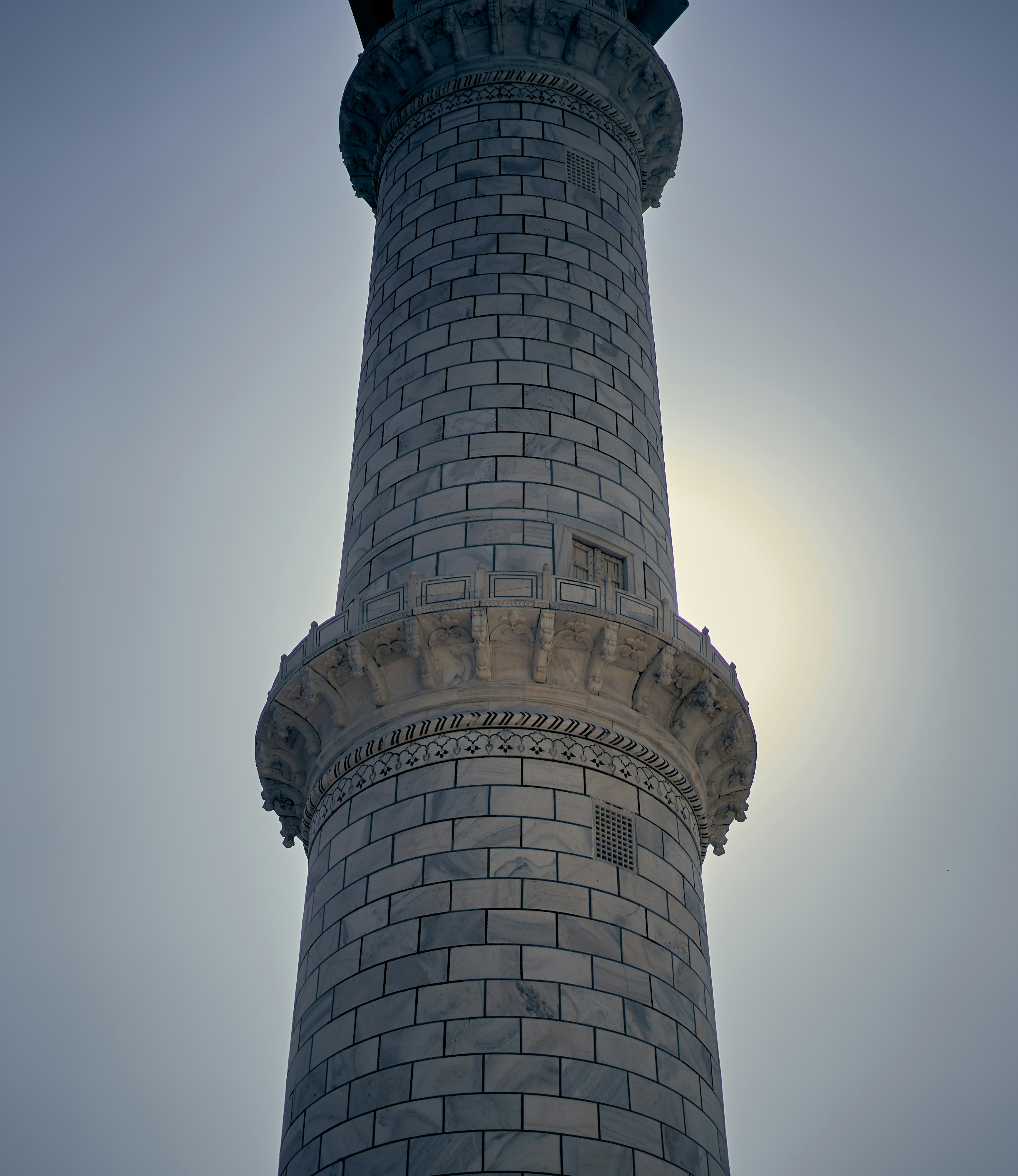 A marble minaret of the Taj Mahal silhouetted against a bright hazy sky.