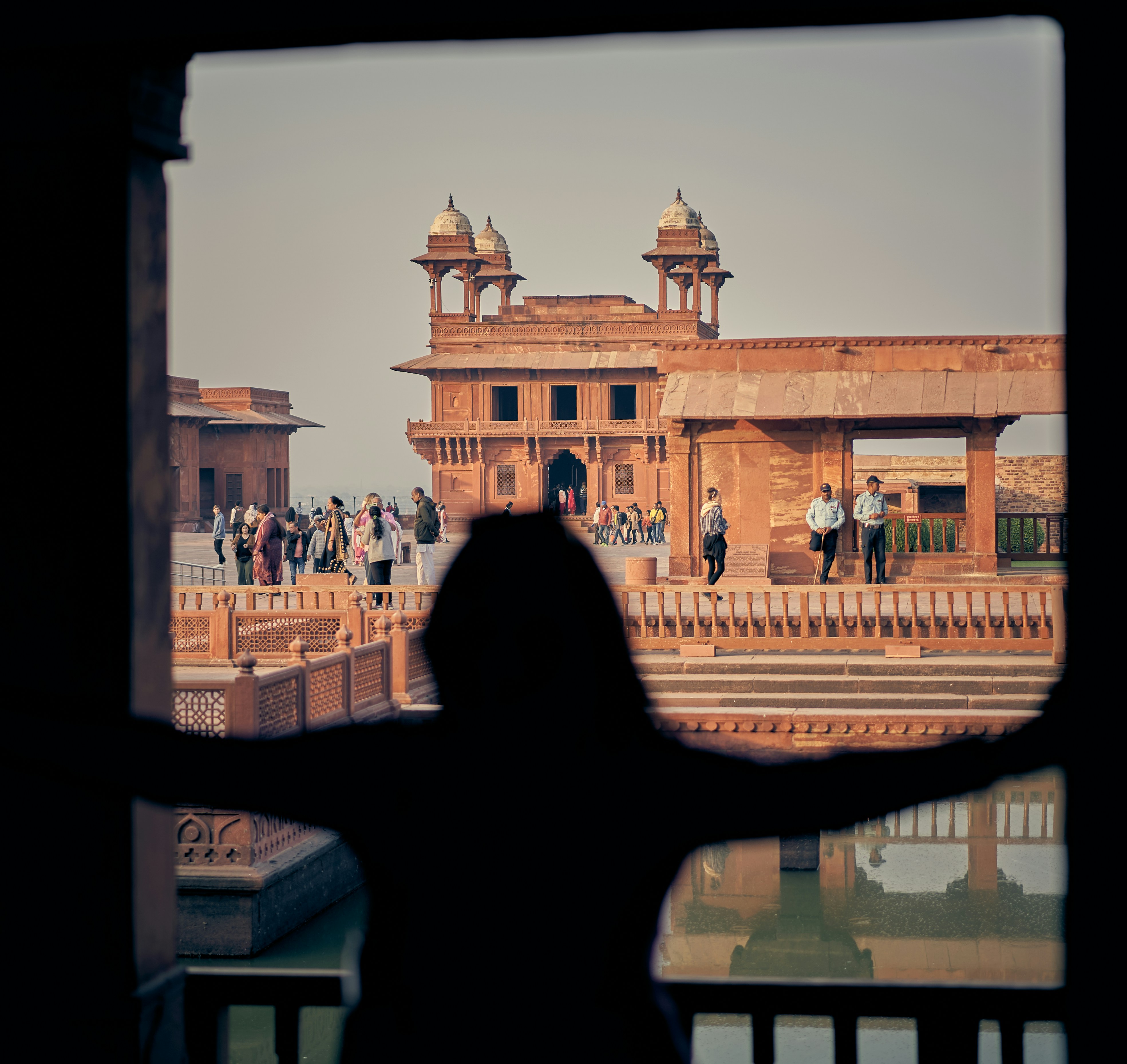 A person in silhouette looking out at the red sandstone architecture of Fatehpur Sikri.