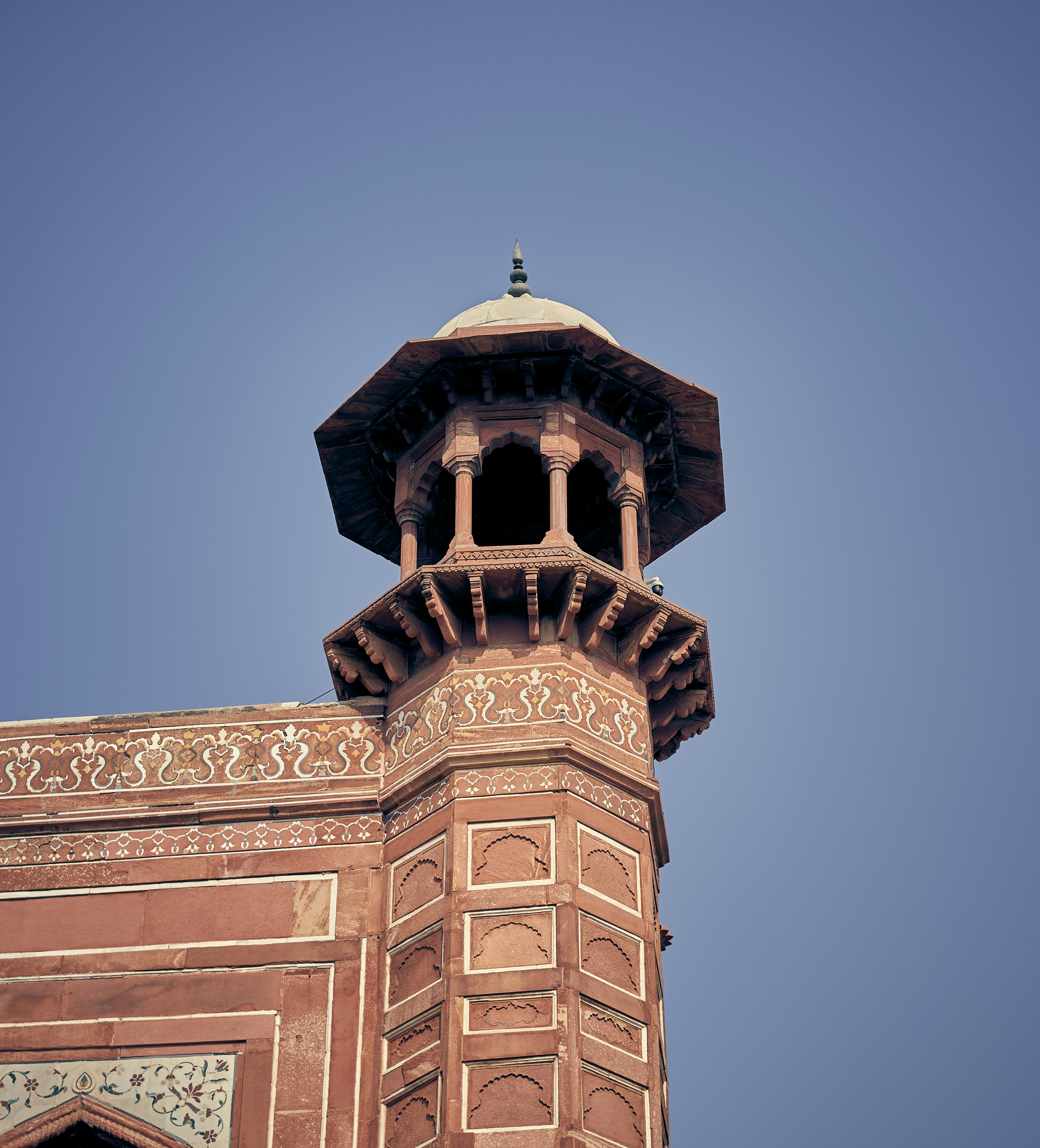 A red sandstone minaret with intricate white inlay against a clear blue sky.