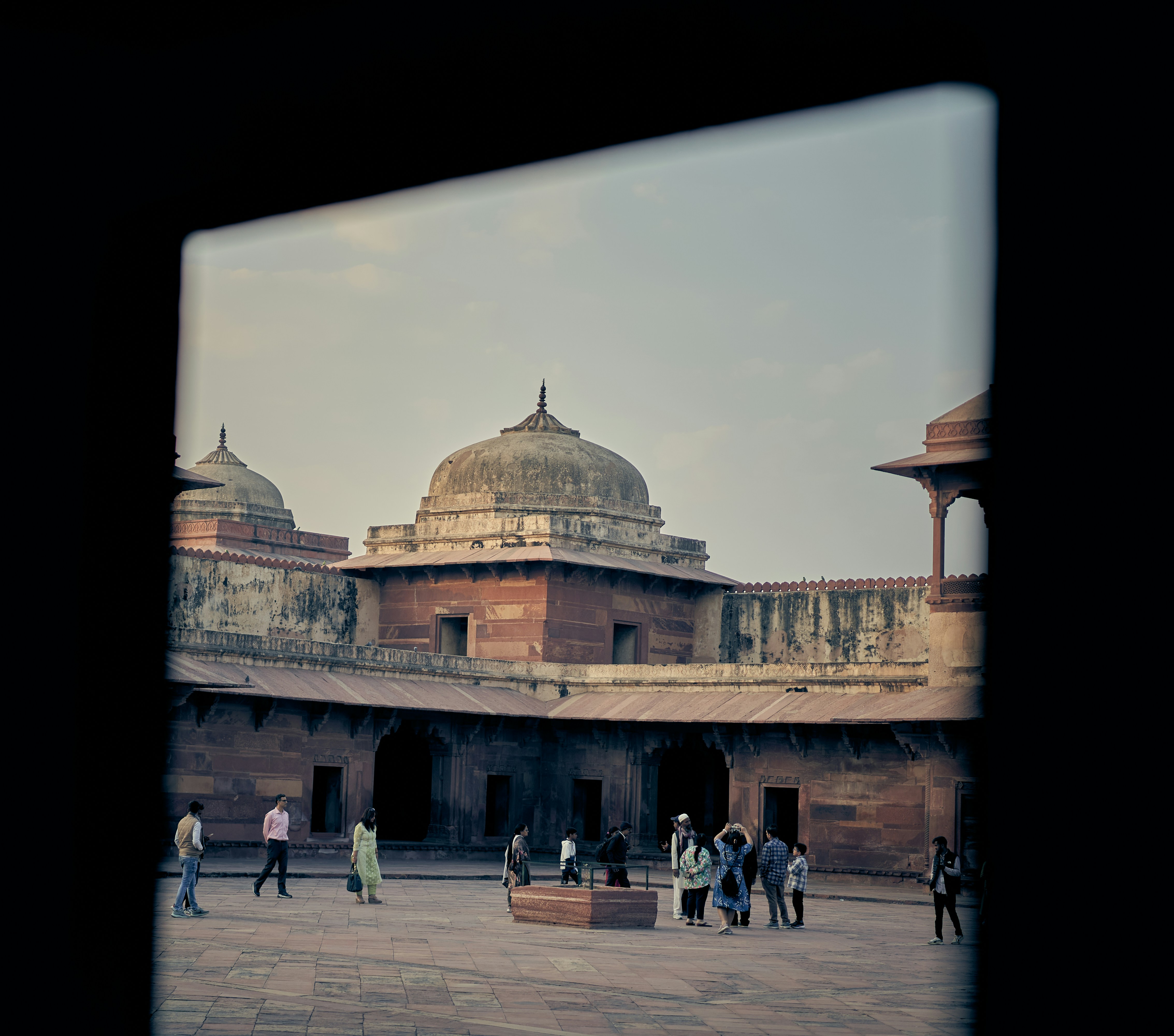 People walking through the red sandstone courtyard of Fatehpur Sikri in India.