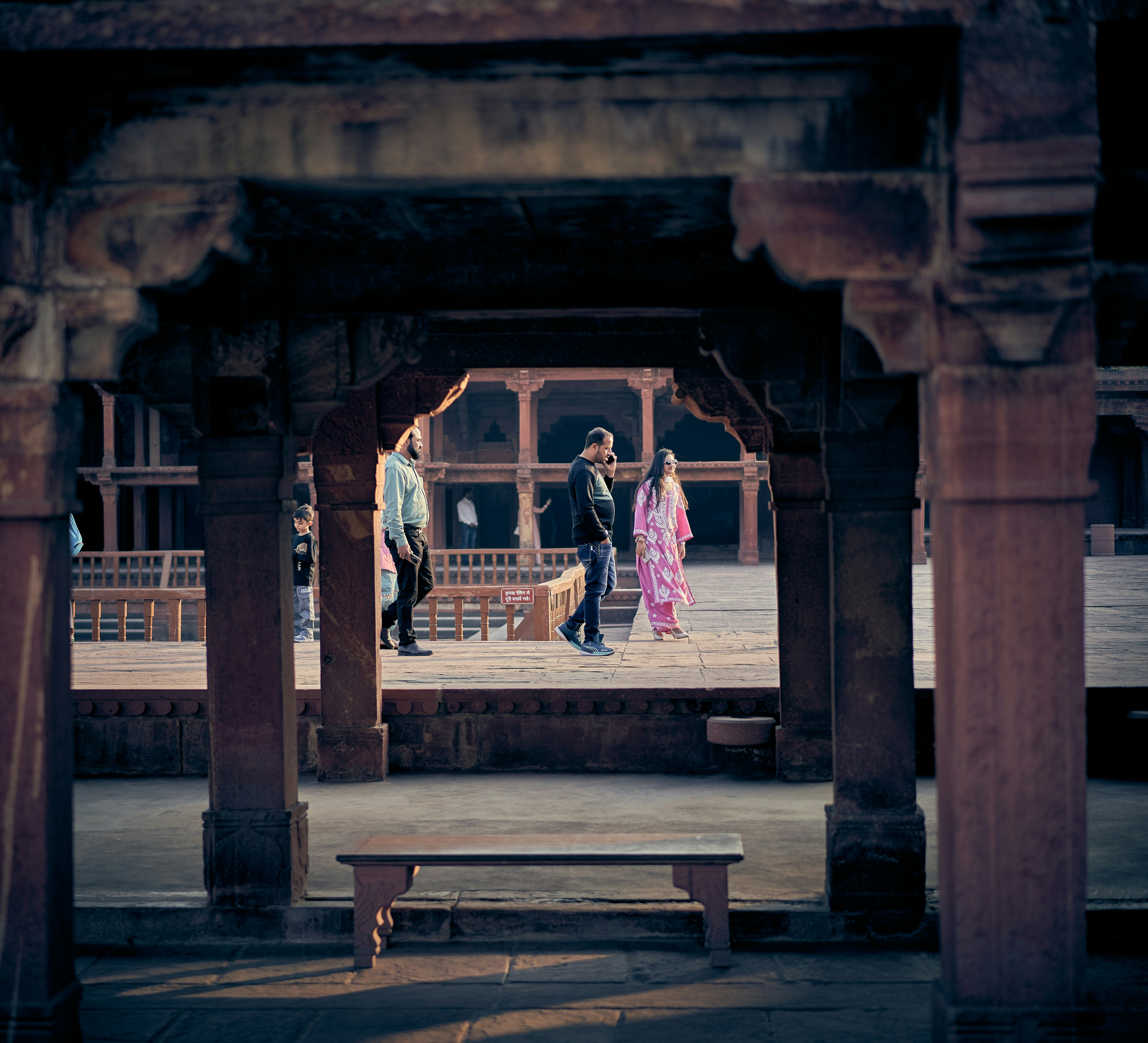 People walking through a stone courtyard with arched pillars at Fatehpur Sikri.