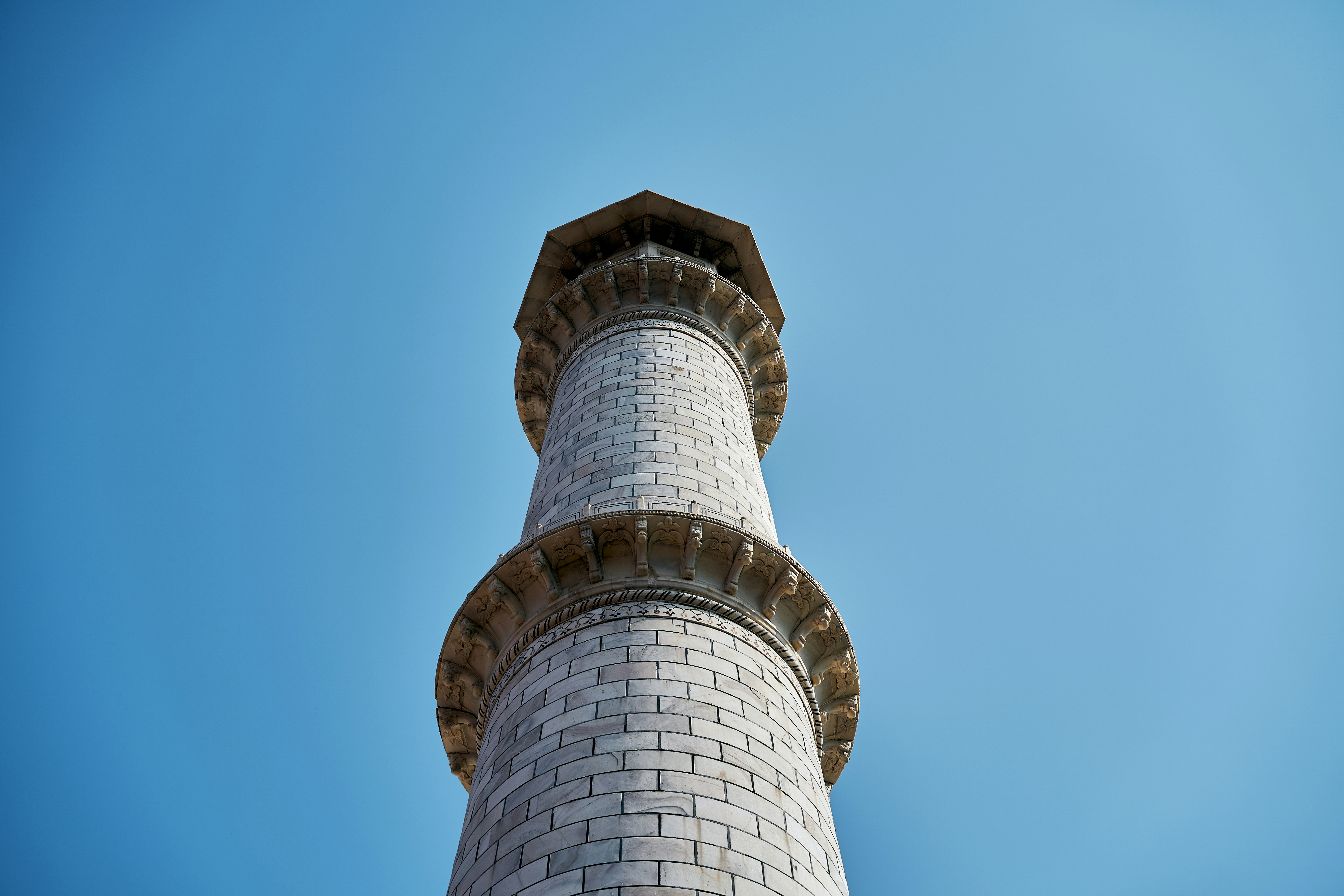 A marble minaret of the Taj Mahal against a clear blue sky.