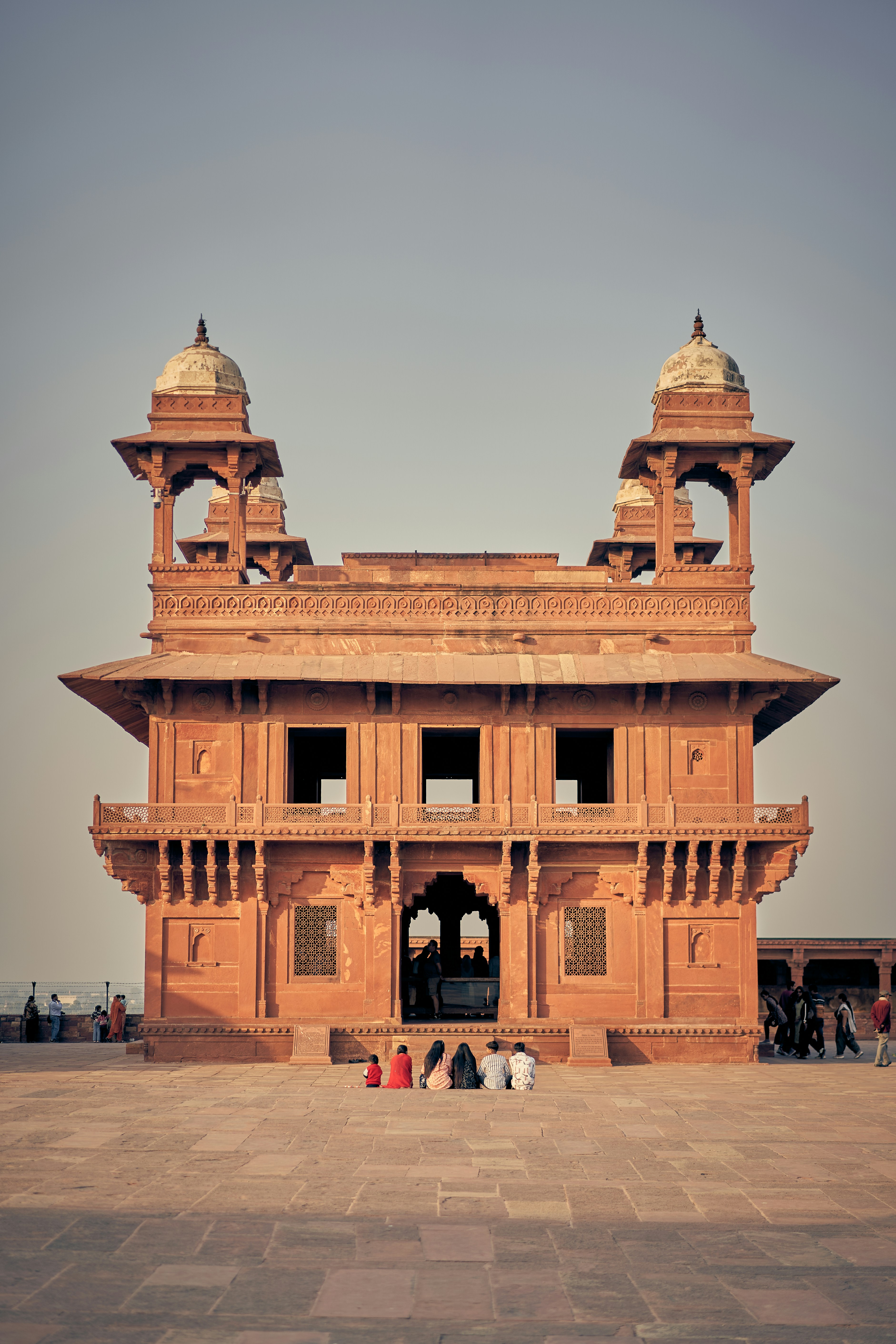 A group of people sitting on a stone courtyard before the Diwan-i-Khas in Fatehpur Sikri.