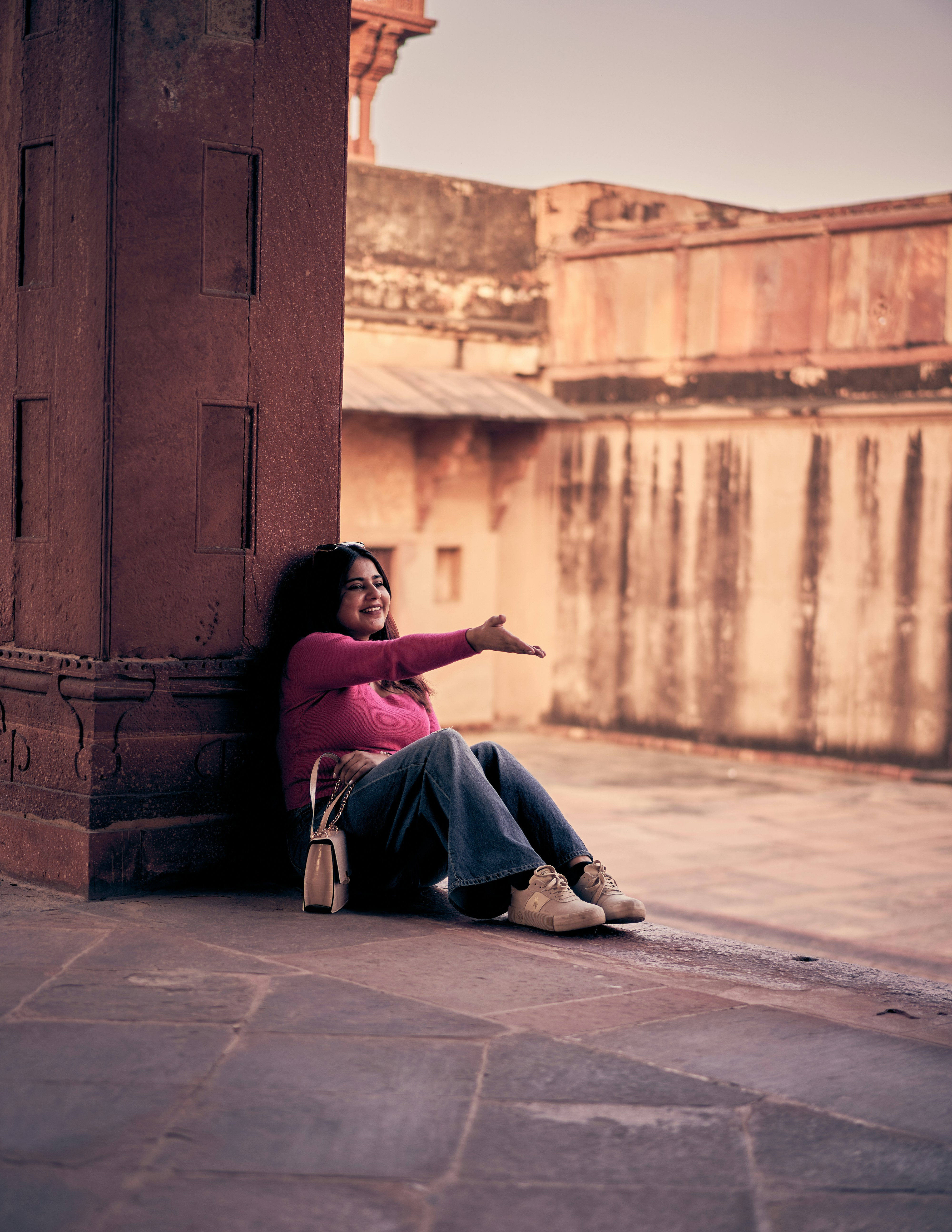 A woman in a pink sweater gesturing while leaning against a red sandstone pillar.