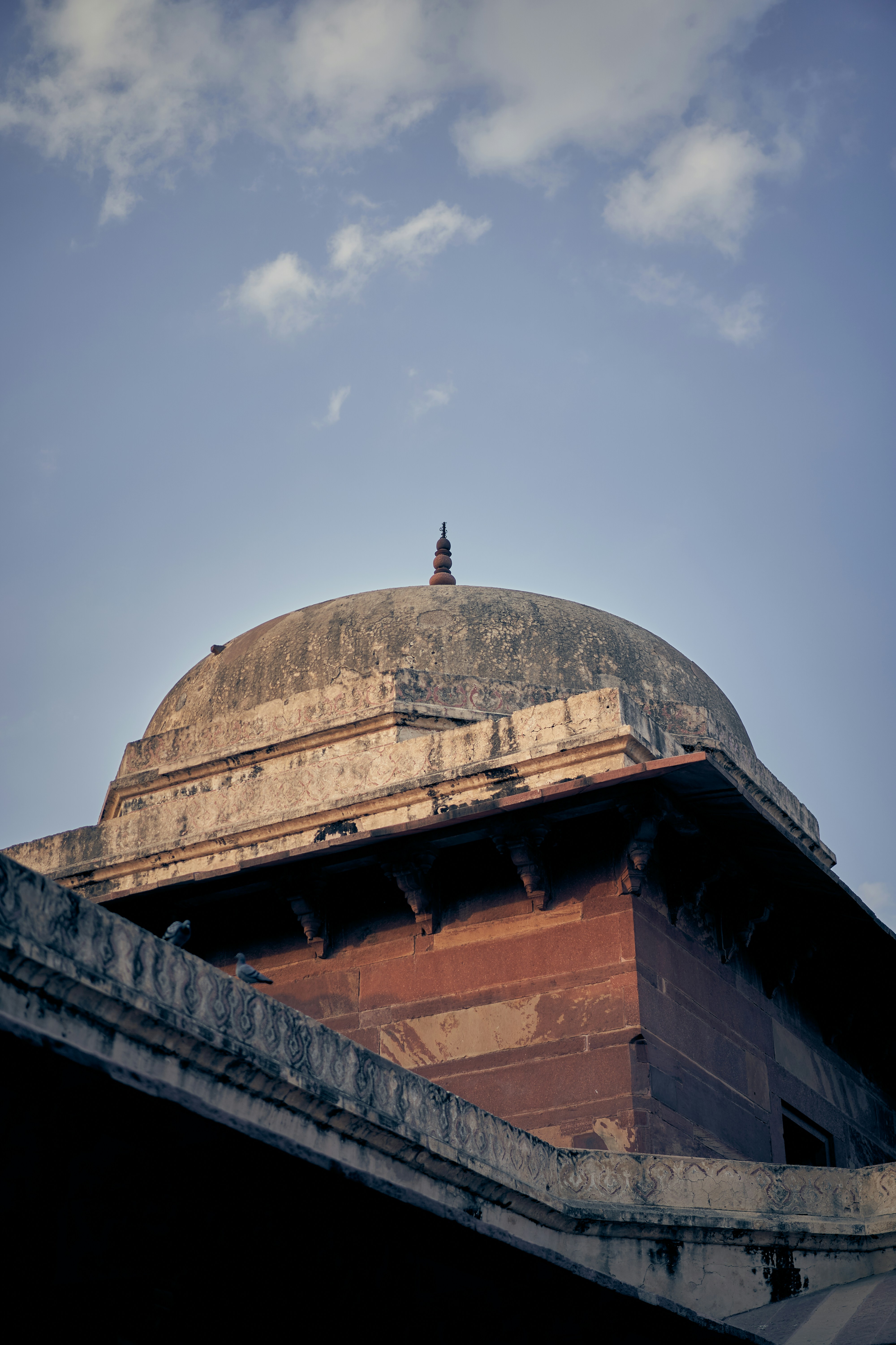 A weathered stone dome with a small finial against a blue sky.