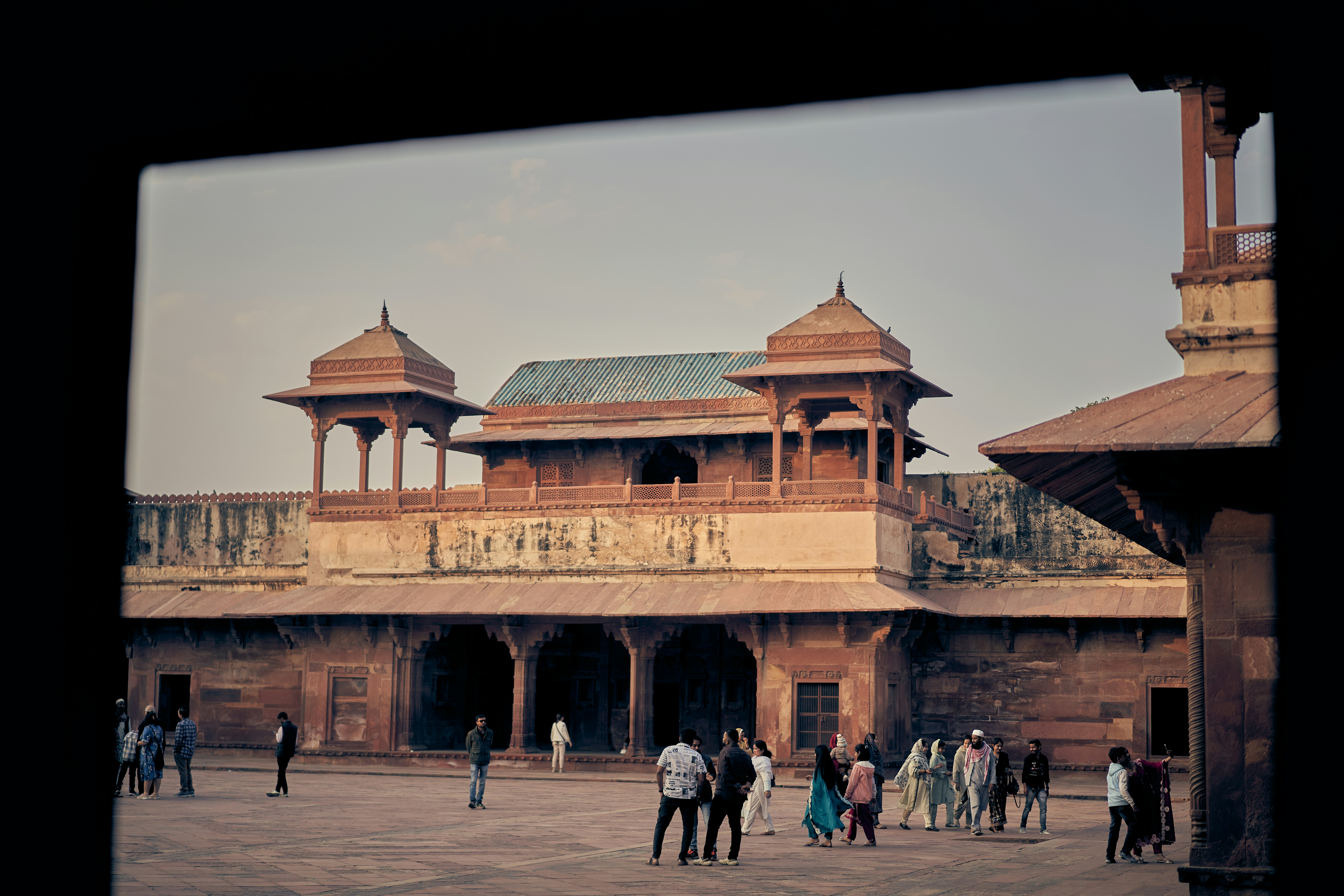 People walking across a courtyard in front of the red sandstone Fatehpur Sikri palace.