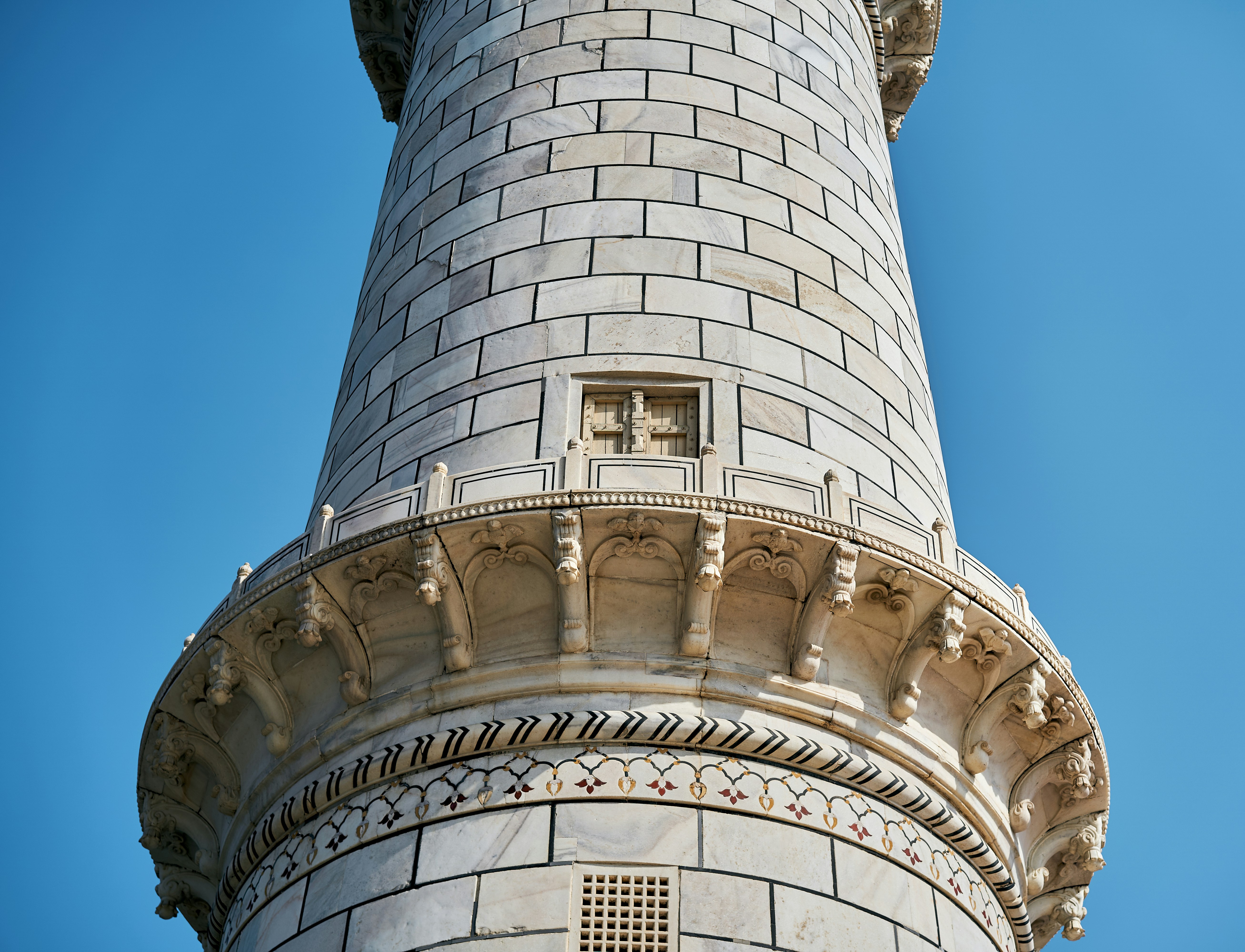 A marble minaret of the Taj Mahal against a clear blue sky in Agra.