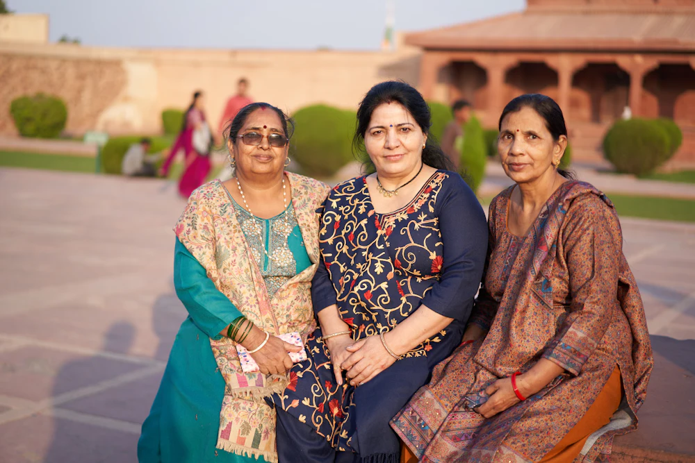 Three women in traditional clothing sitting together in a sunlit courtyard