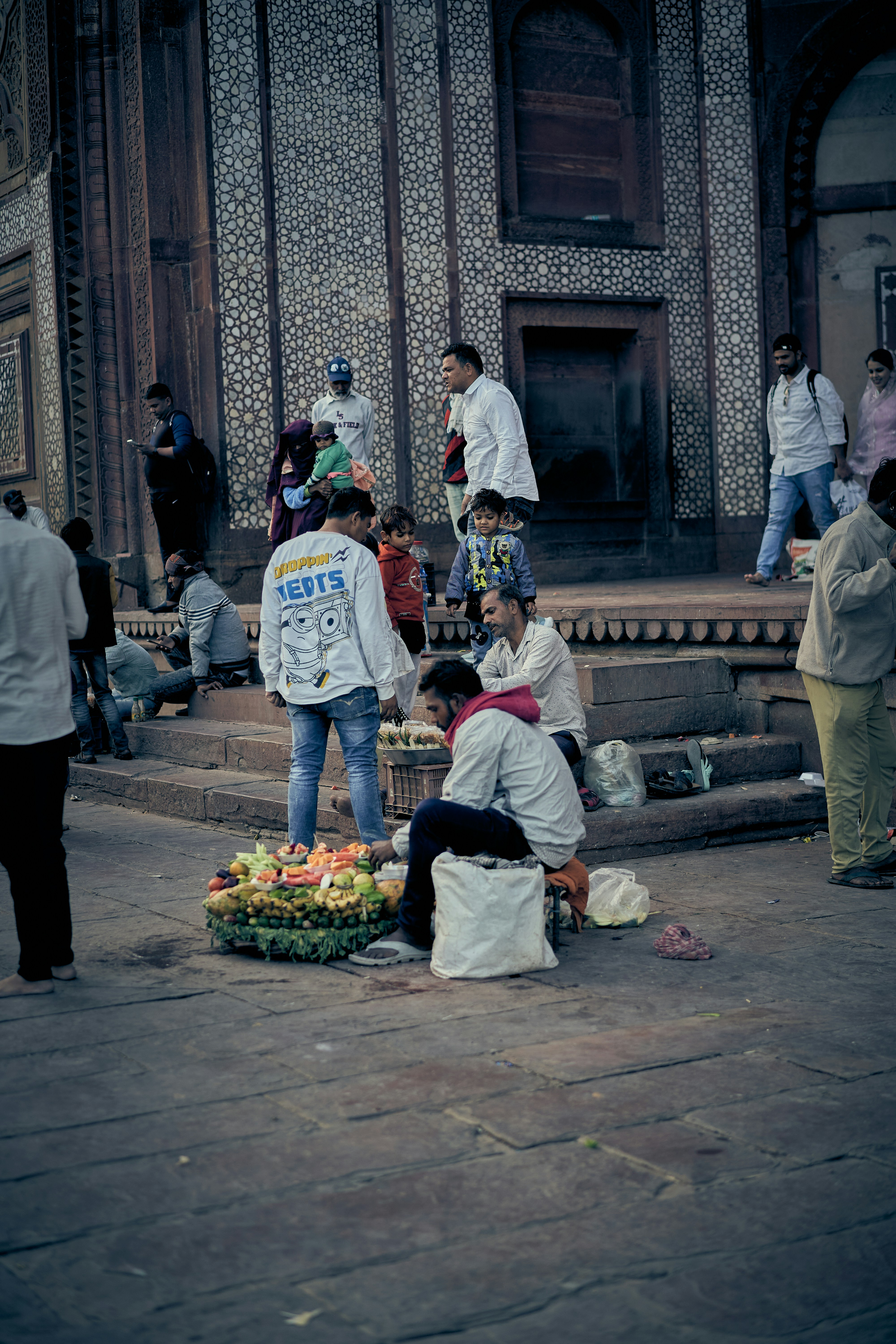 A fruit vendor selling produce on a stone plaza in front of a building.