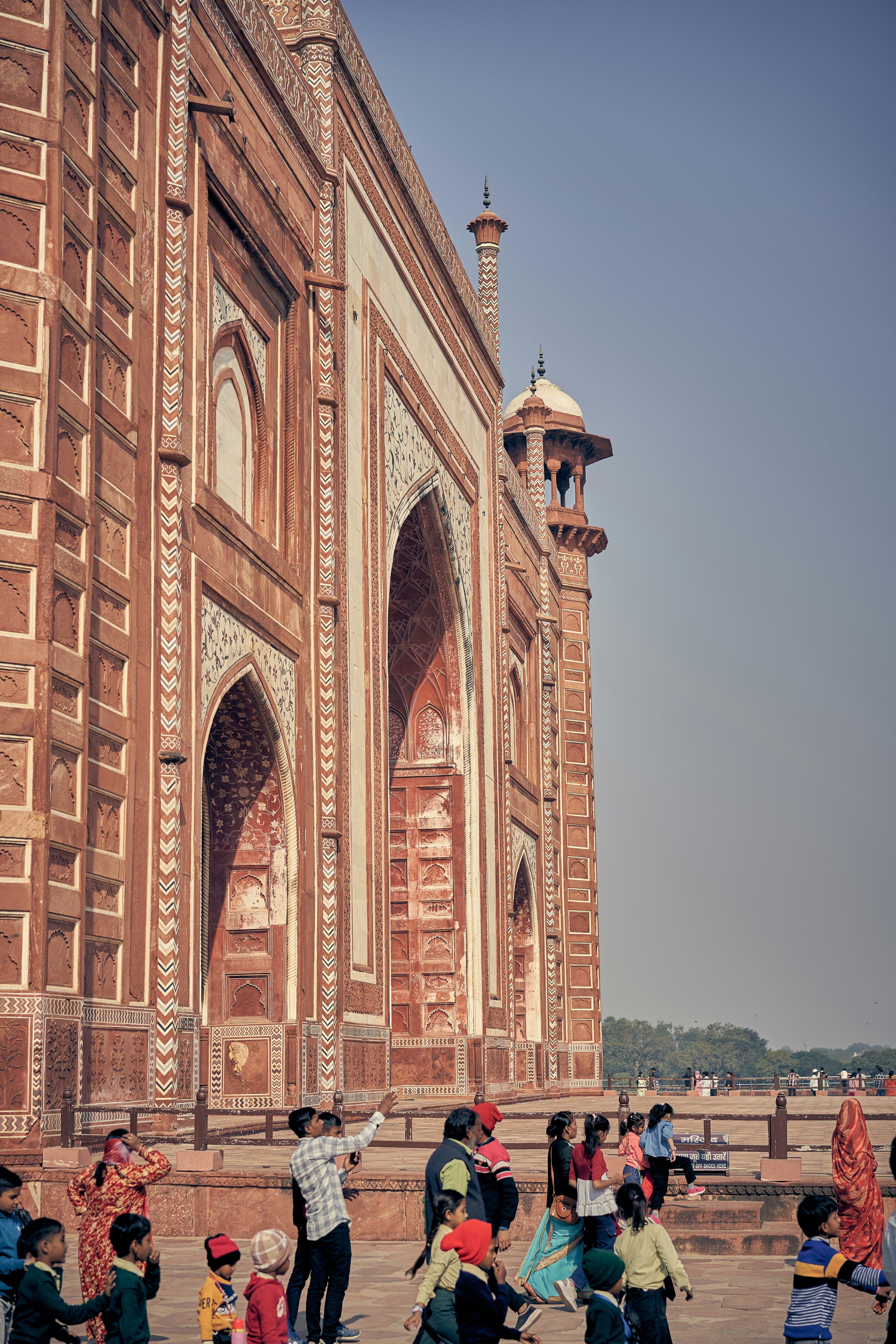 A group of people walking near the red sandstone walls of the Taj Mahal.