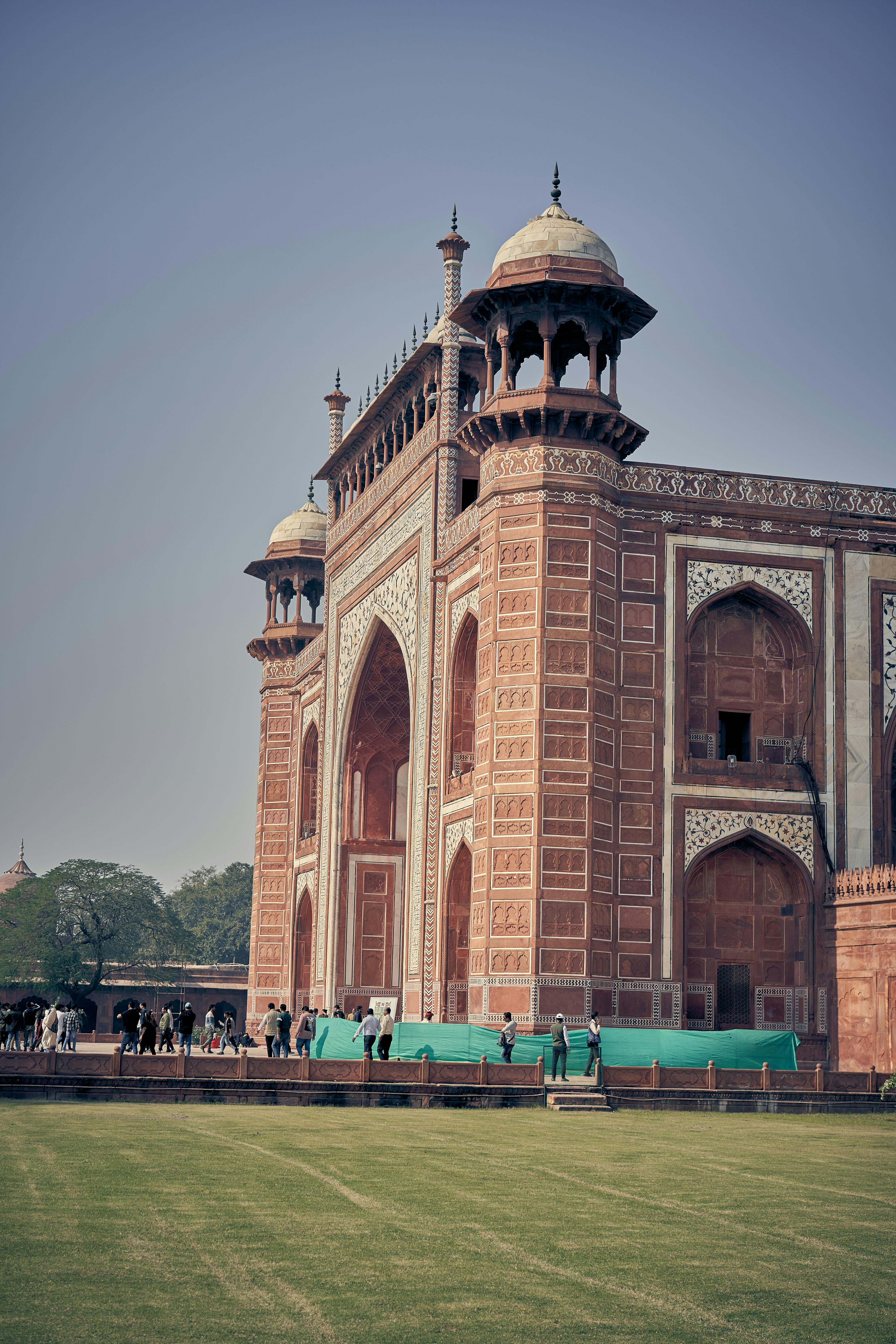The red sandstone gate of the Taj Mahal in Agra with visitors walking nearby.