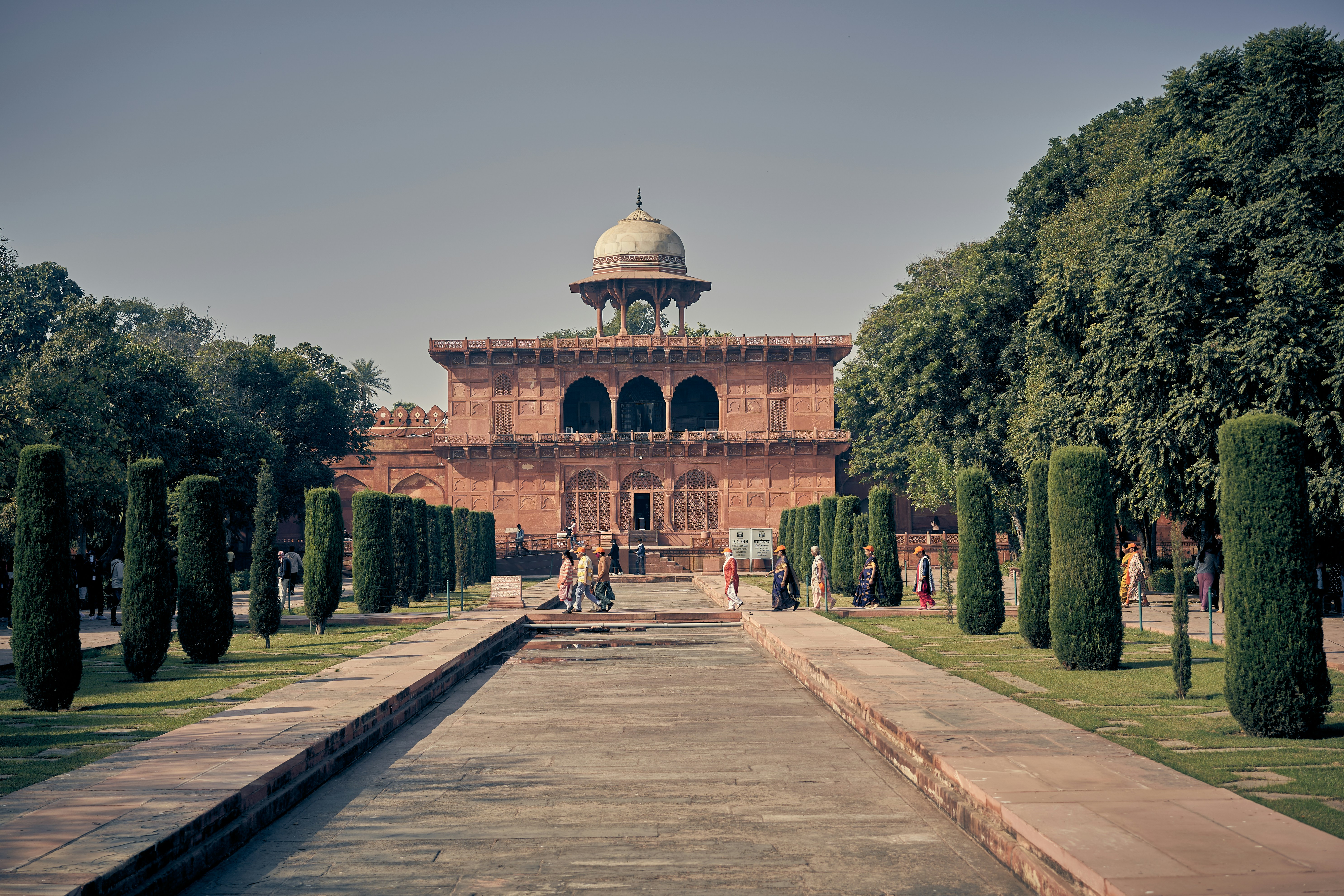 People walking along a stone path toward the red sandstone Taj Mahal complex.