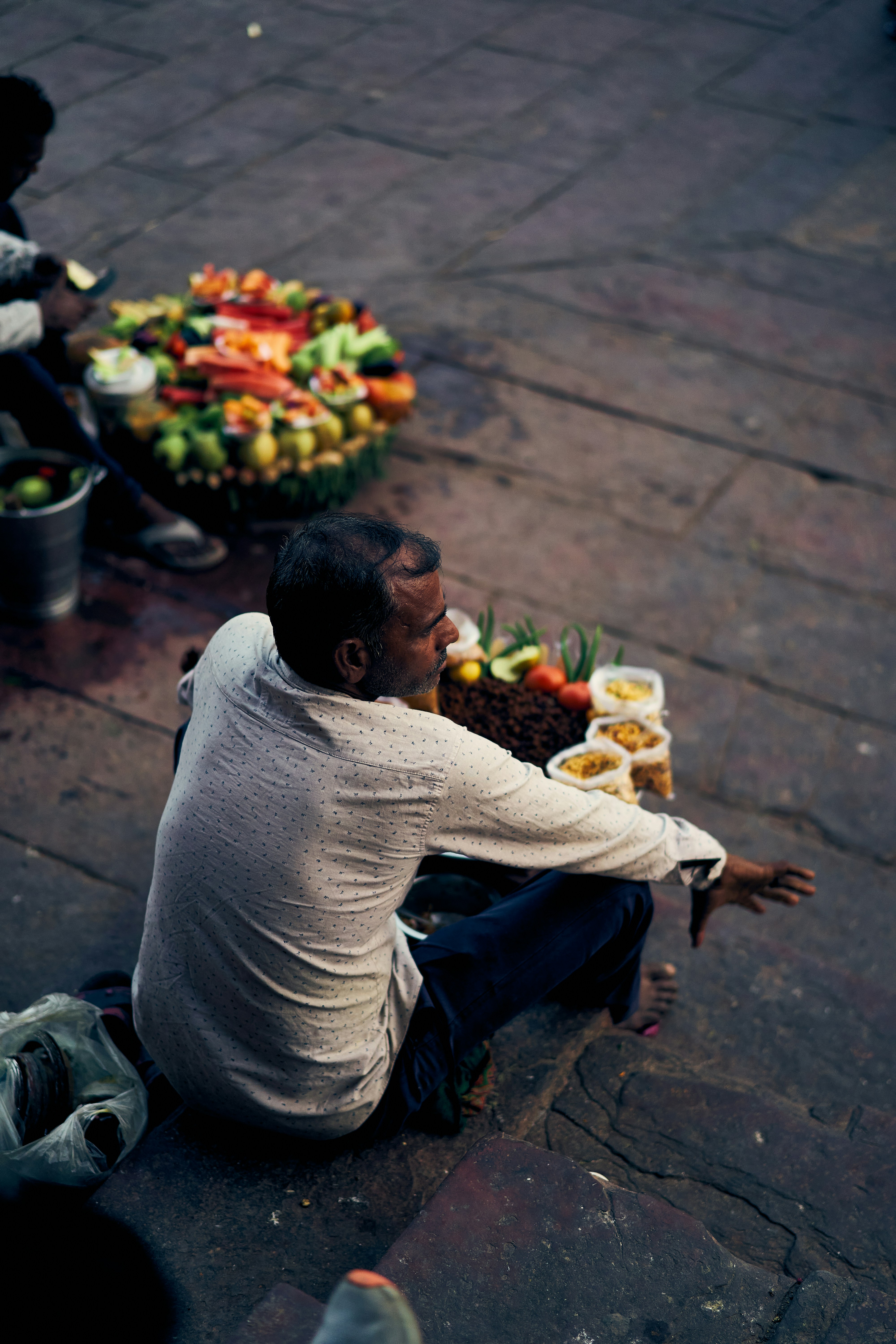 A man in a light shirt sitting on stone steps beside food containers.