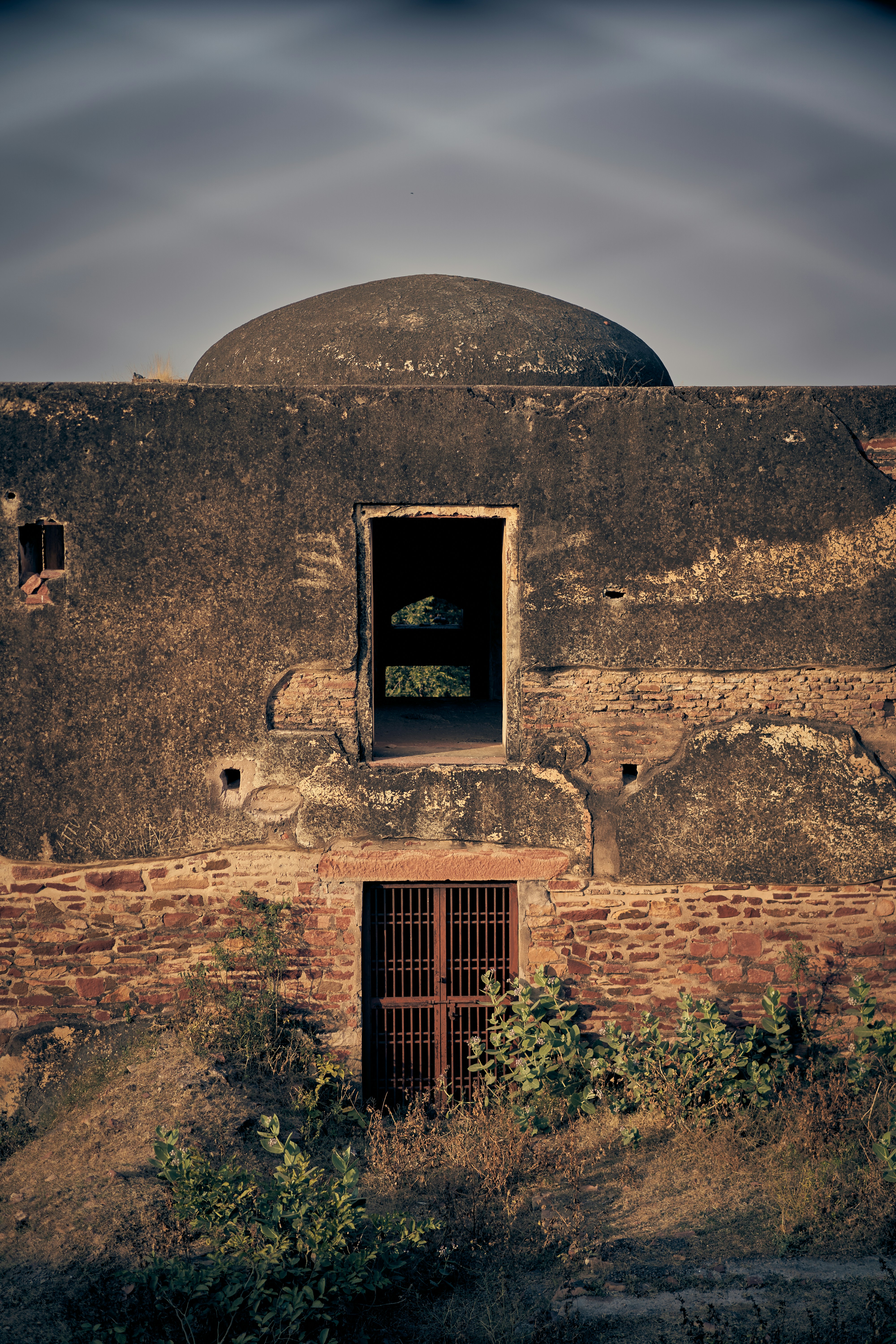 An old stone building with a domed roof, arched doorway, and metal gate.