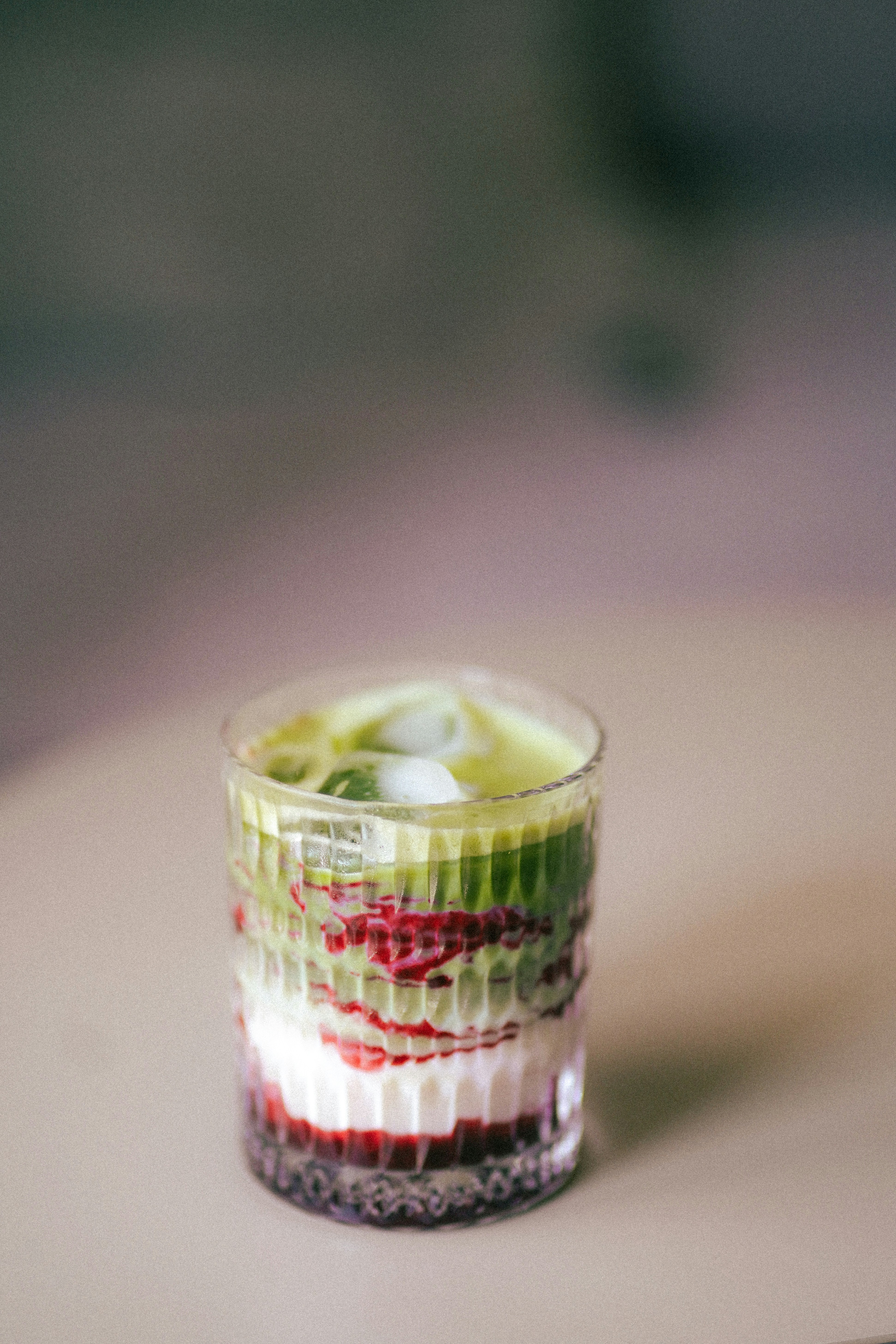 A layered iced matcha latte with red berry syrup in a textured glass.