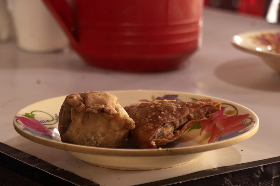 Samosas on a floral plate with a red teapot