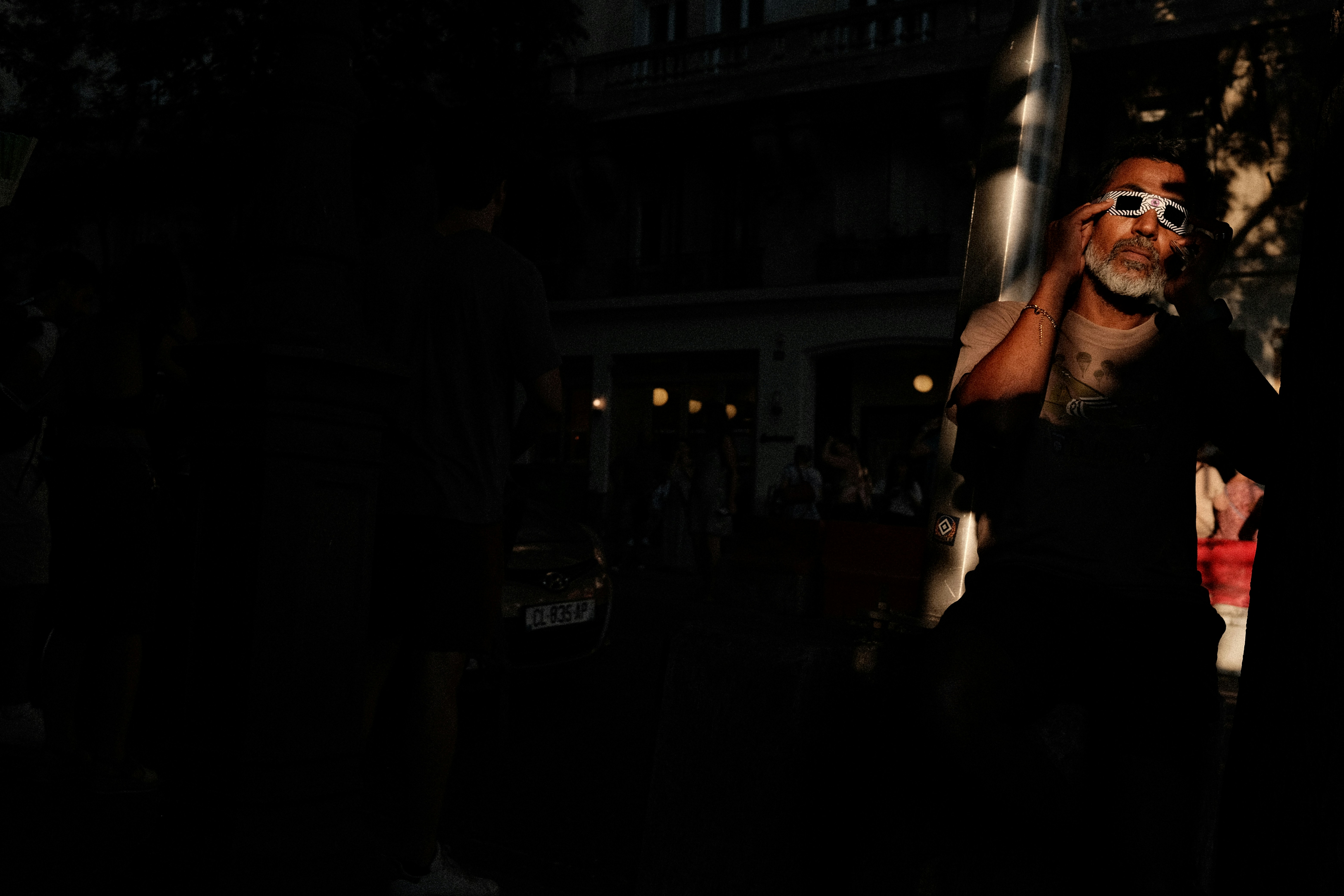 A man with a grey beard wearing eclipse glasses on a city street