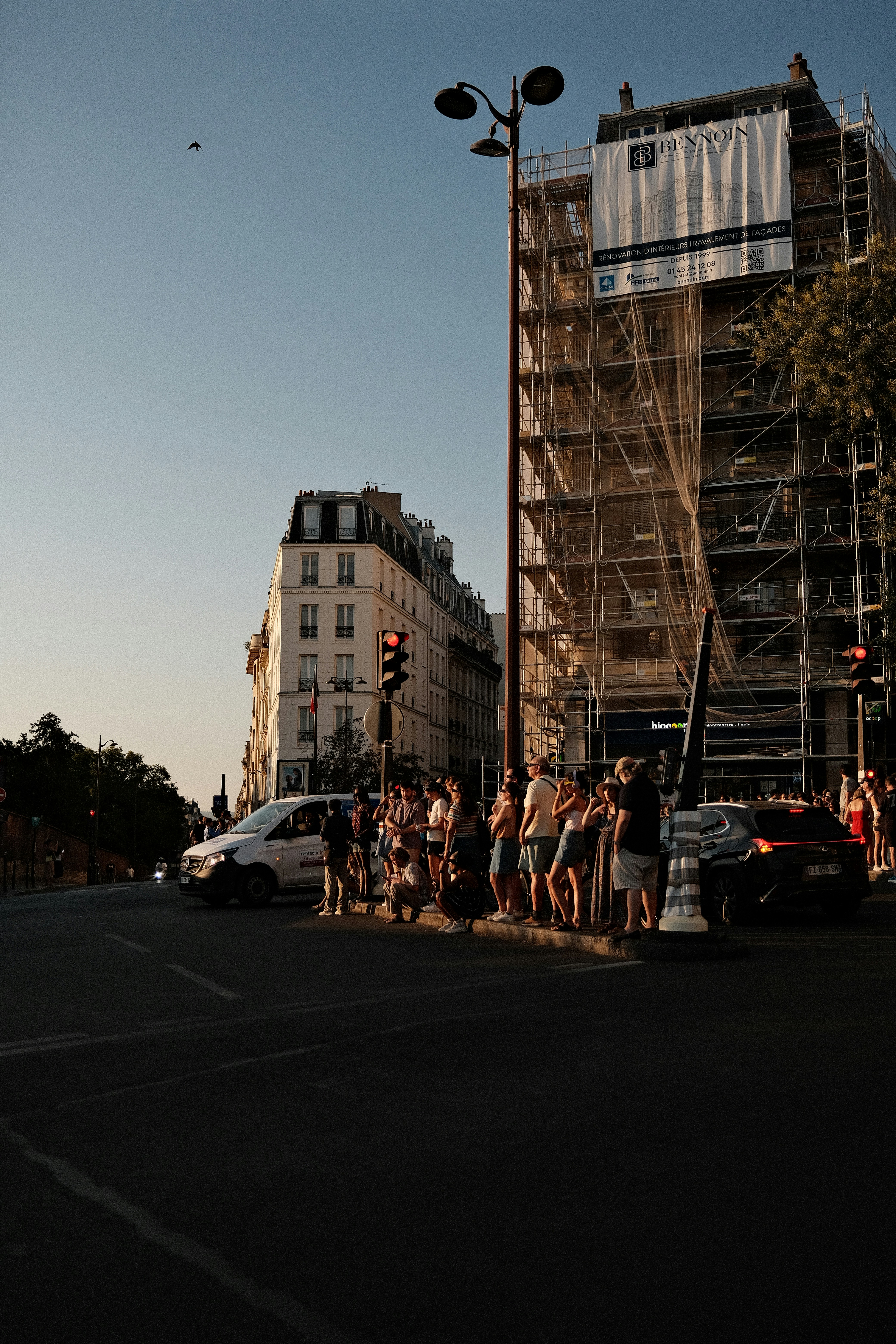A group of people waiting at a street corner in Paris at golden hour.