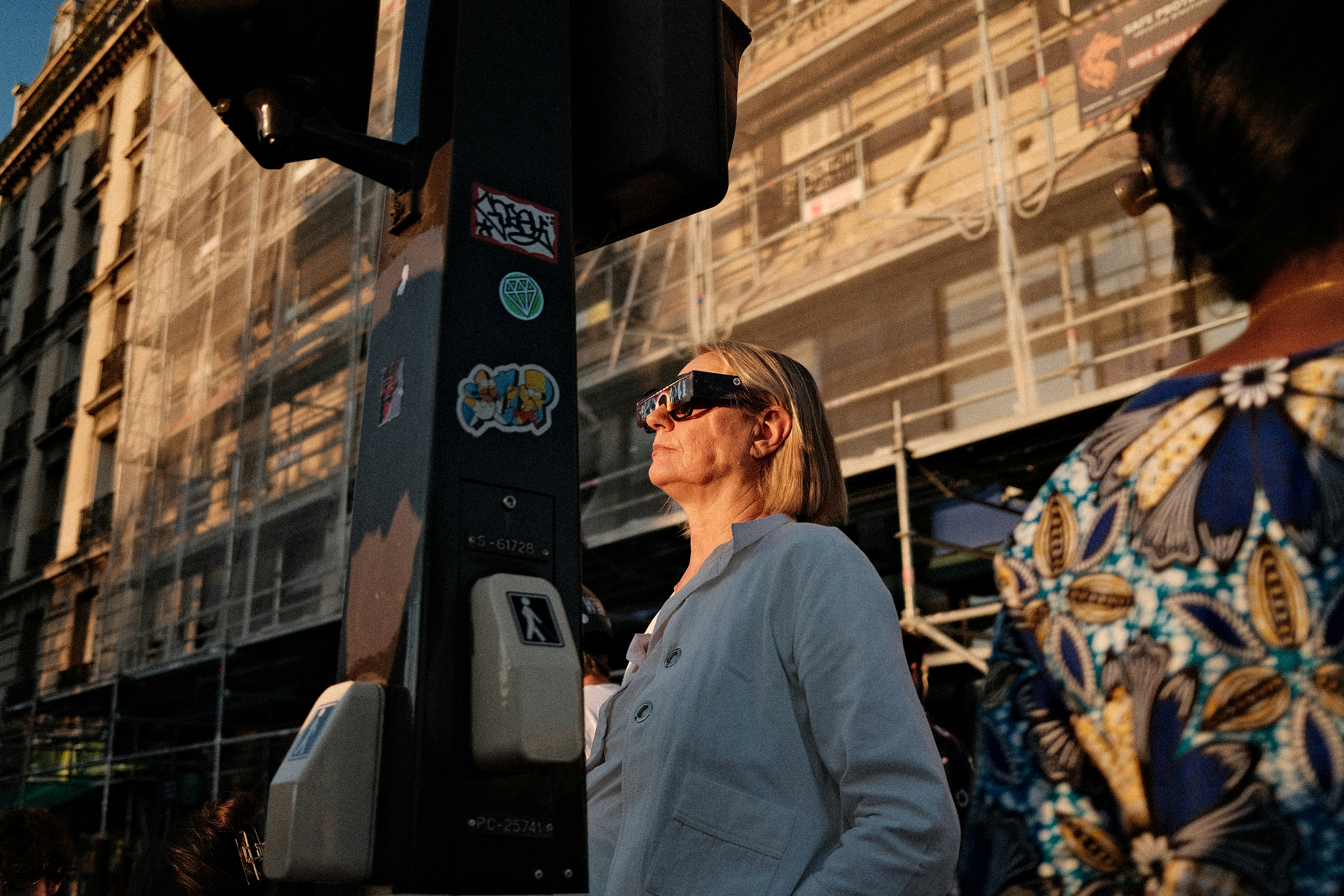 A woman wearing eclipse glasses on a city street during the golden hour.