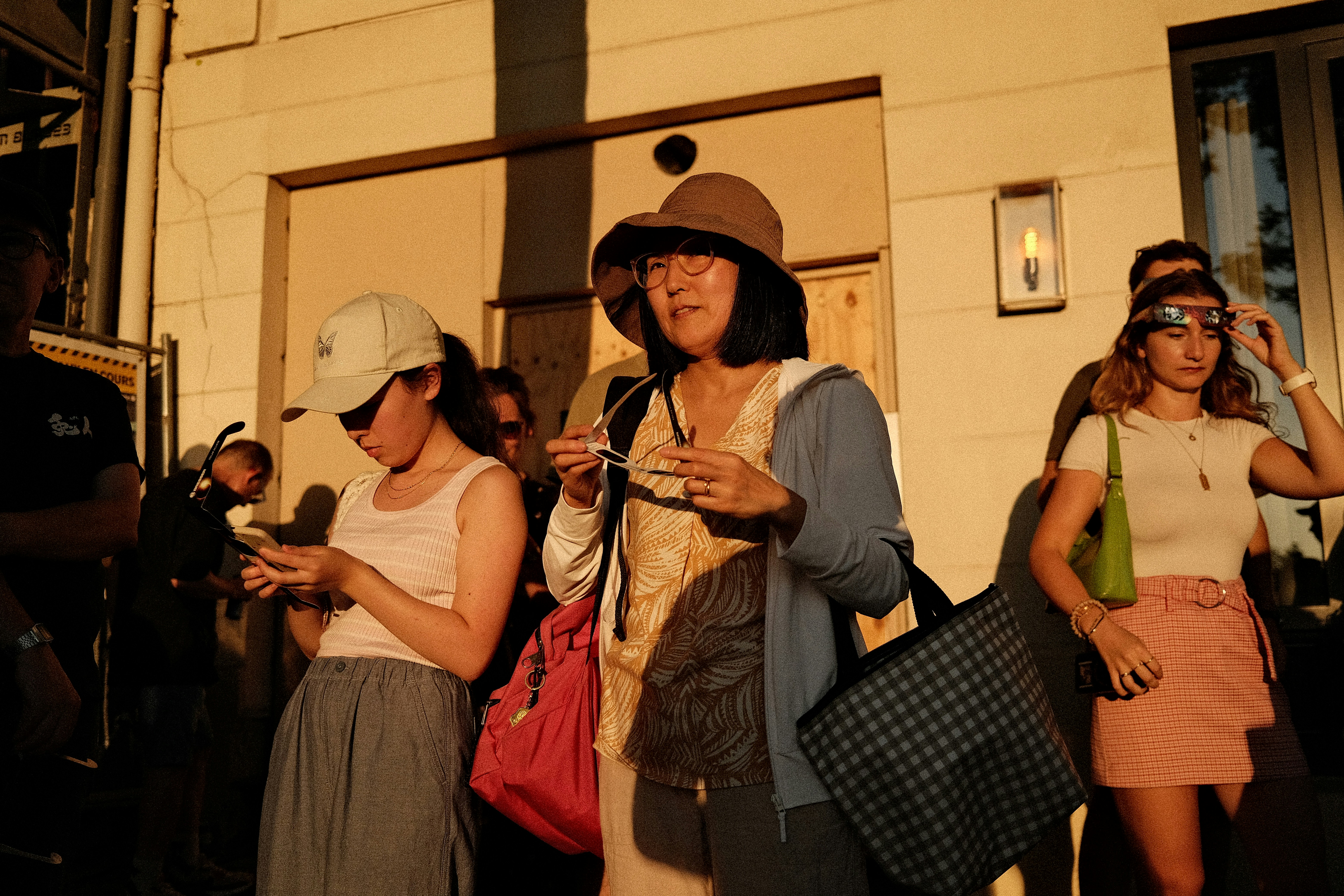 A group of people in golden hour light holding eclipse glasses outside a building.