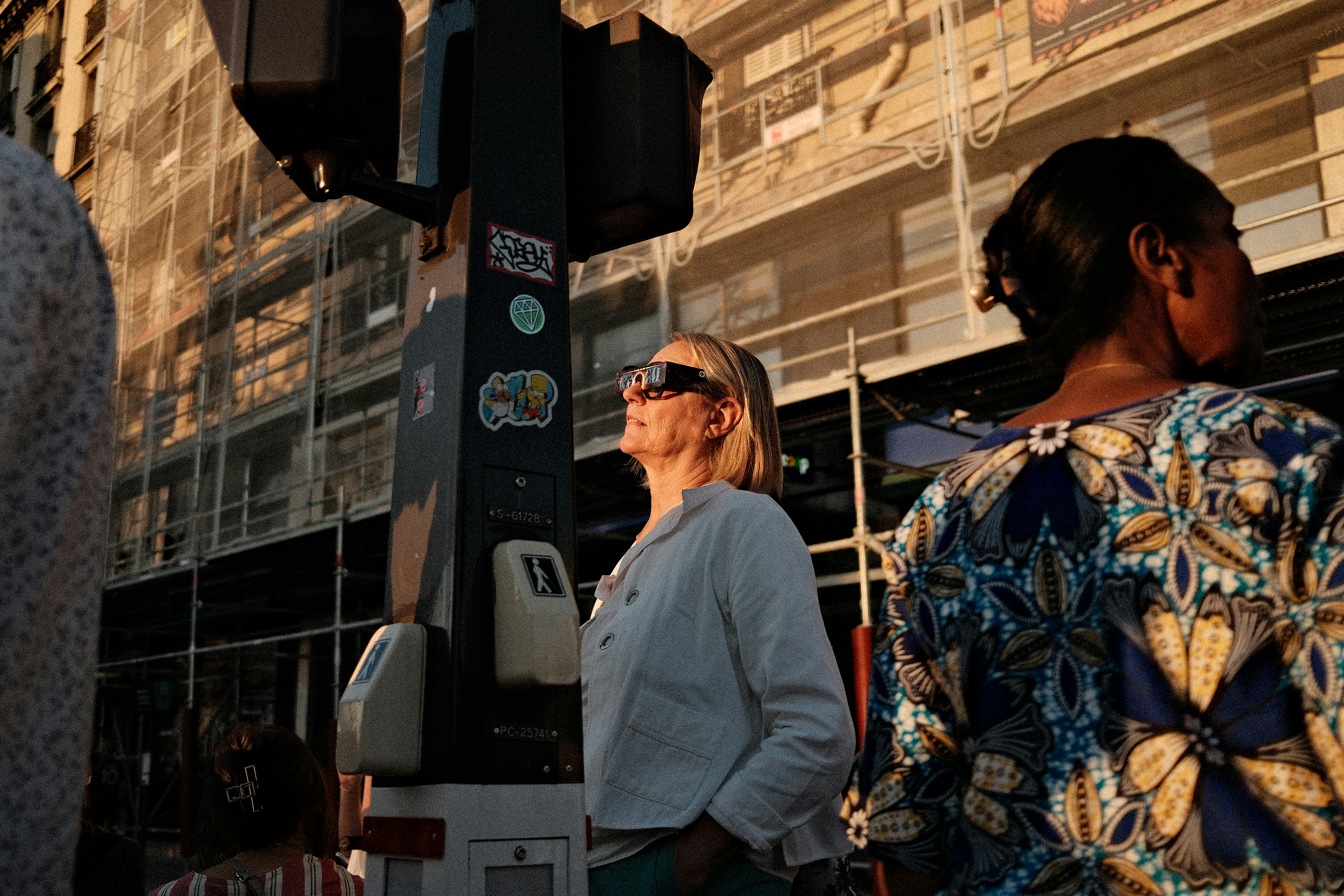 A woman wearing eclipse glasses on a city street during the golden hour